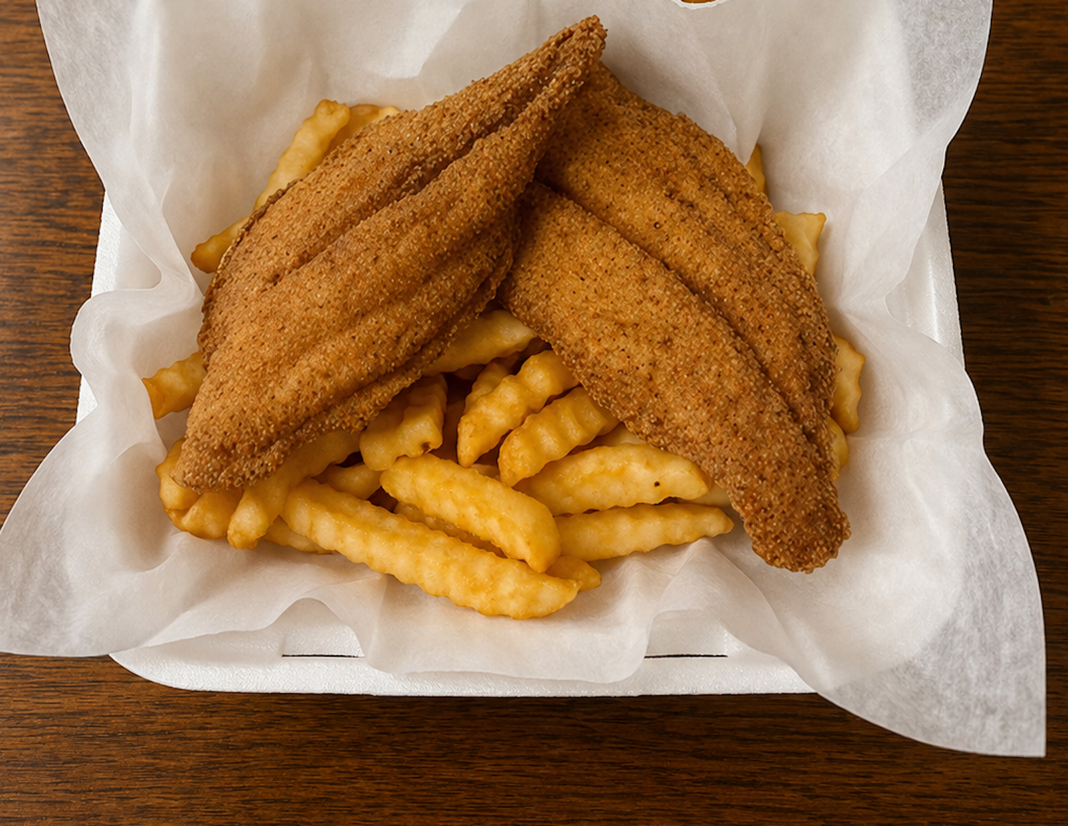 Fried fish fillets with crinkle-cut French fries on white paper in a basket