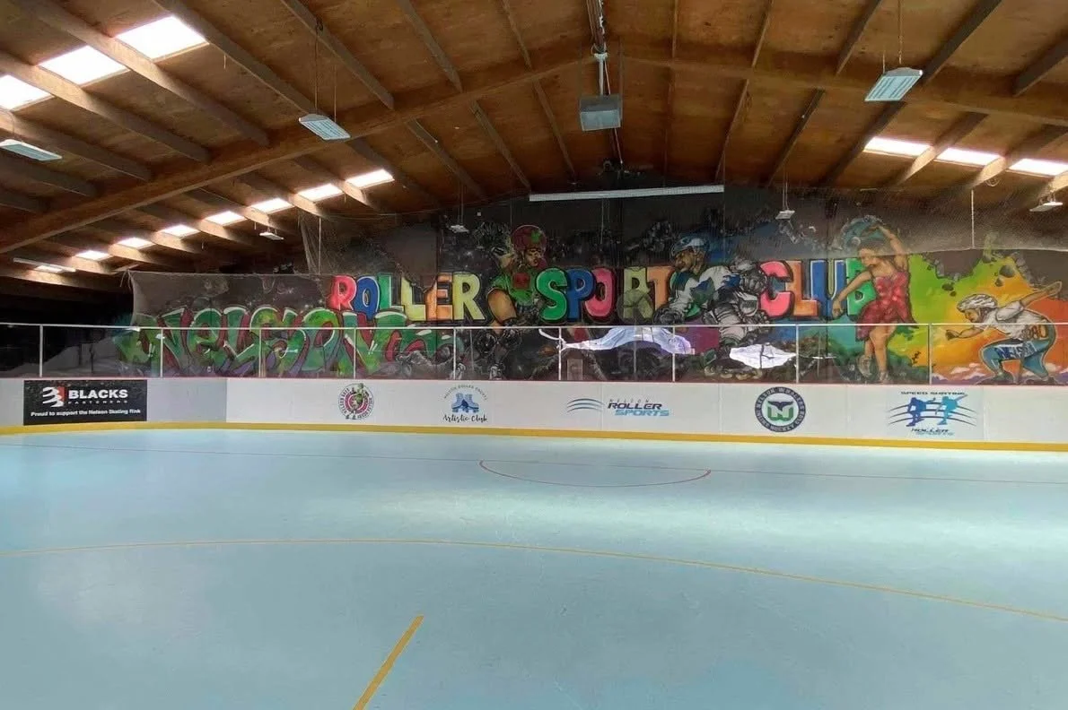 Indoor roller hockey rink with a colorful graffiti mural on the wall featuring children roller skating and riding bikes, with the words 'ROLLER SPORT CLUB' in large letters.