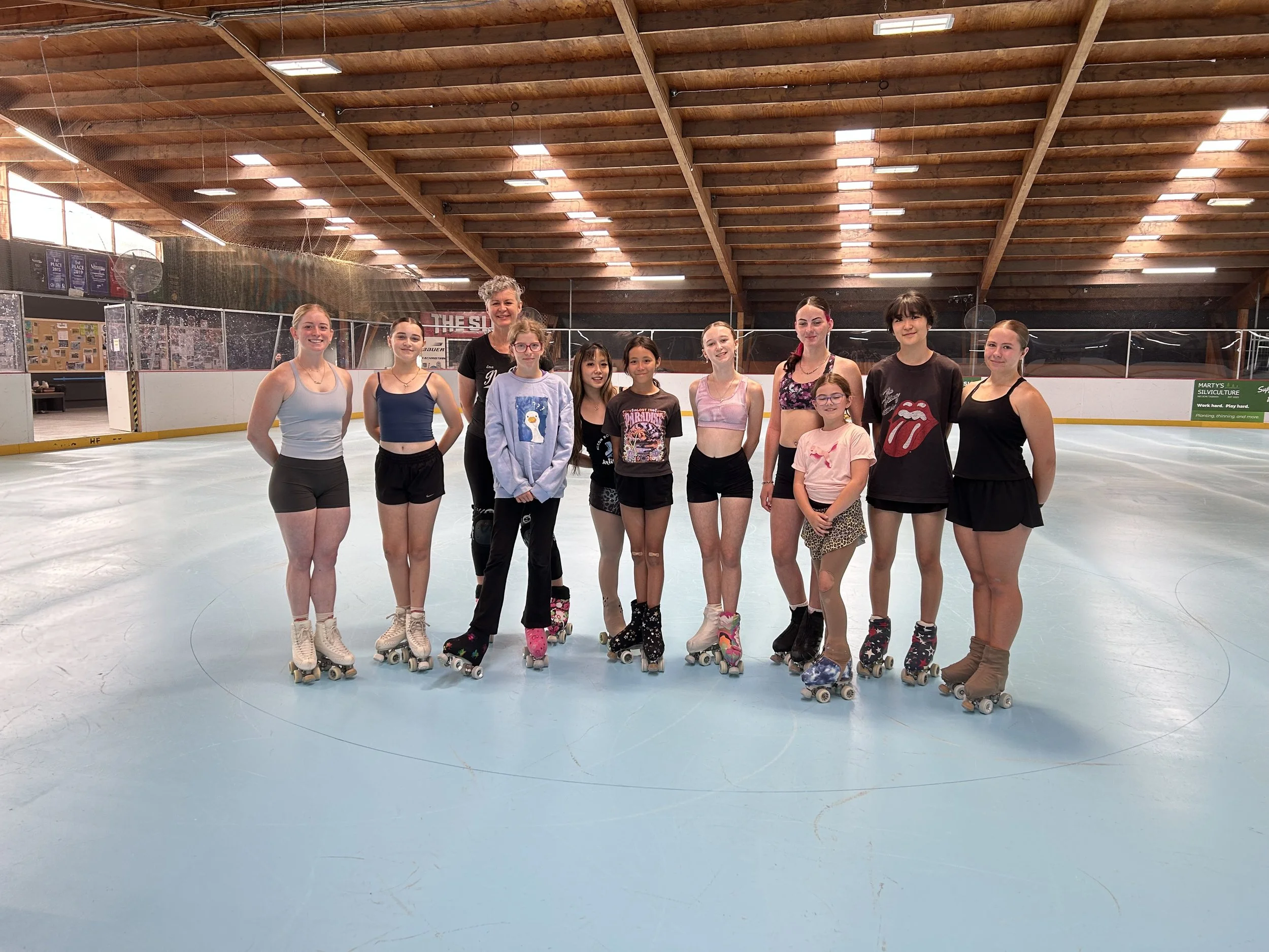 A group of skaters standing together on an indoor roller skating rink, all wearing skating outfits, smiling for the camera.