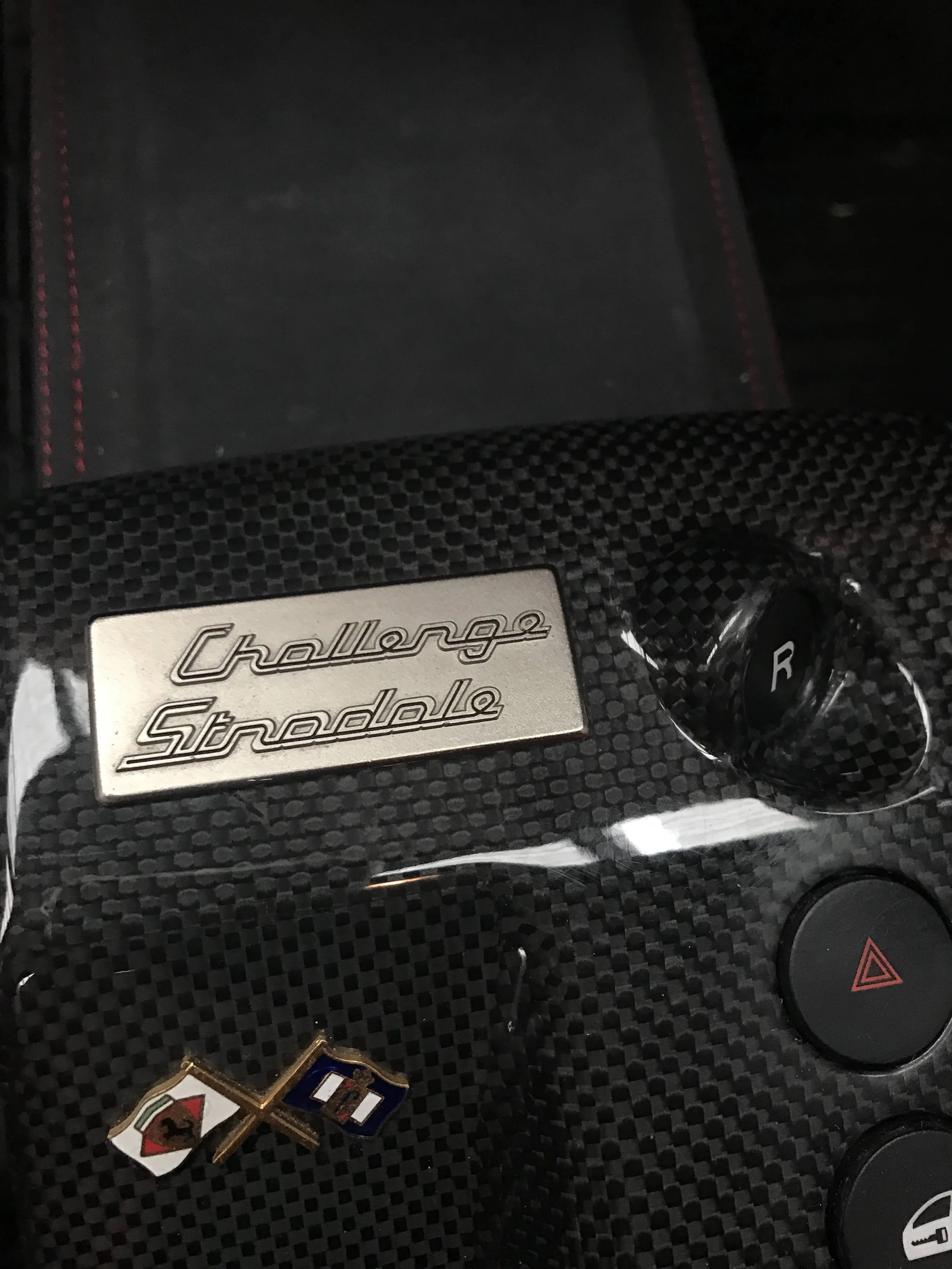 Close-up of a car dashboard with a metallic emblem reading 'Challenger SRT', some automotive pins, and car control buttons.