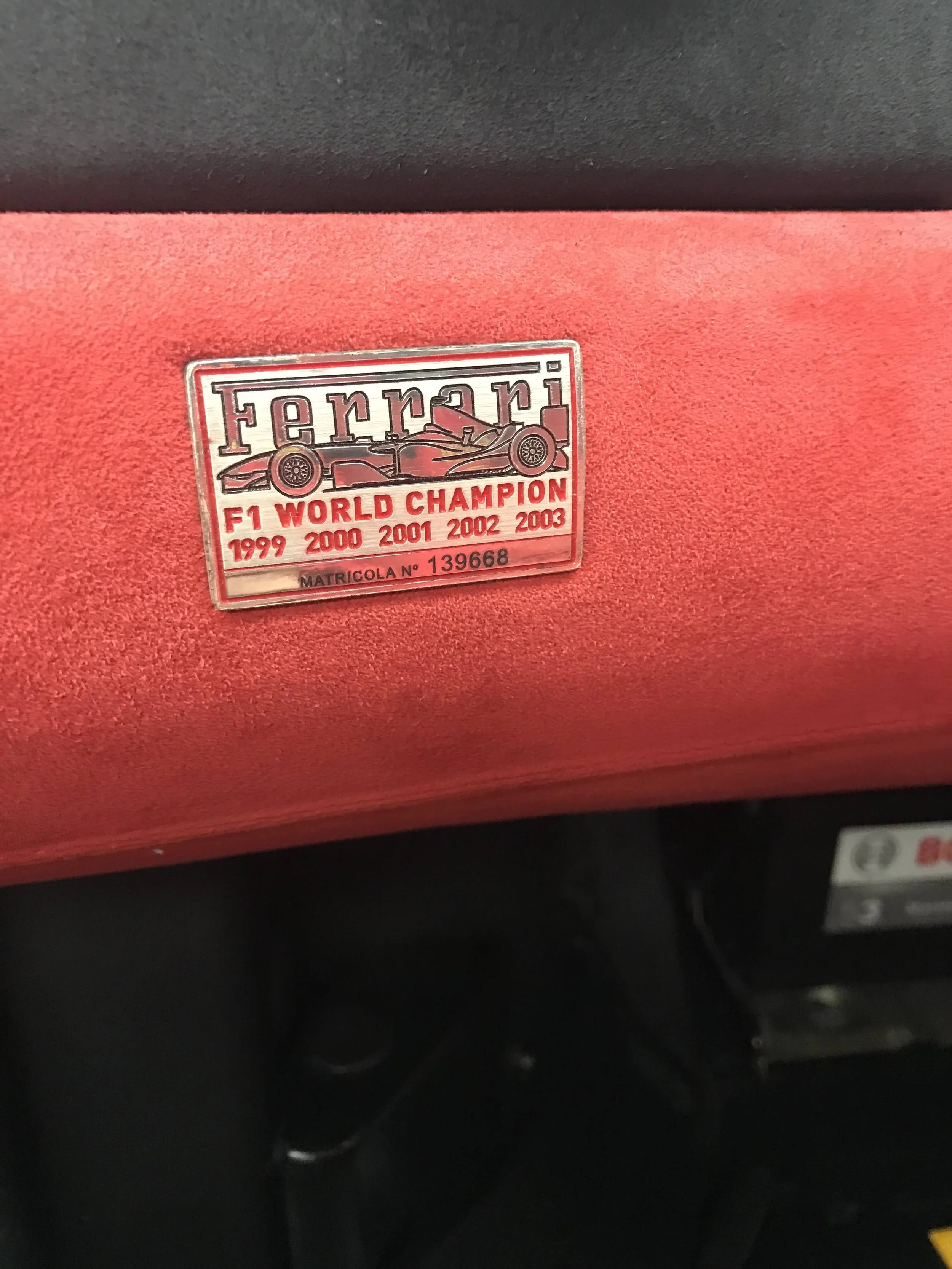 Close-up of a plaque on a red Ferrari car, indicating the model was a F1 World Champion in 1999, 2000, 2001, 2002, and 2003.