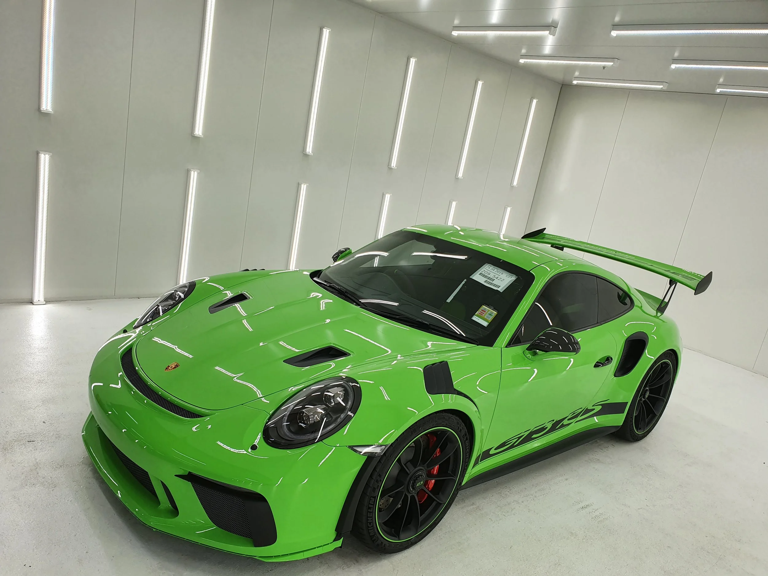 A bright green sports car parked in a clean, white indoor garage with modern lighting.