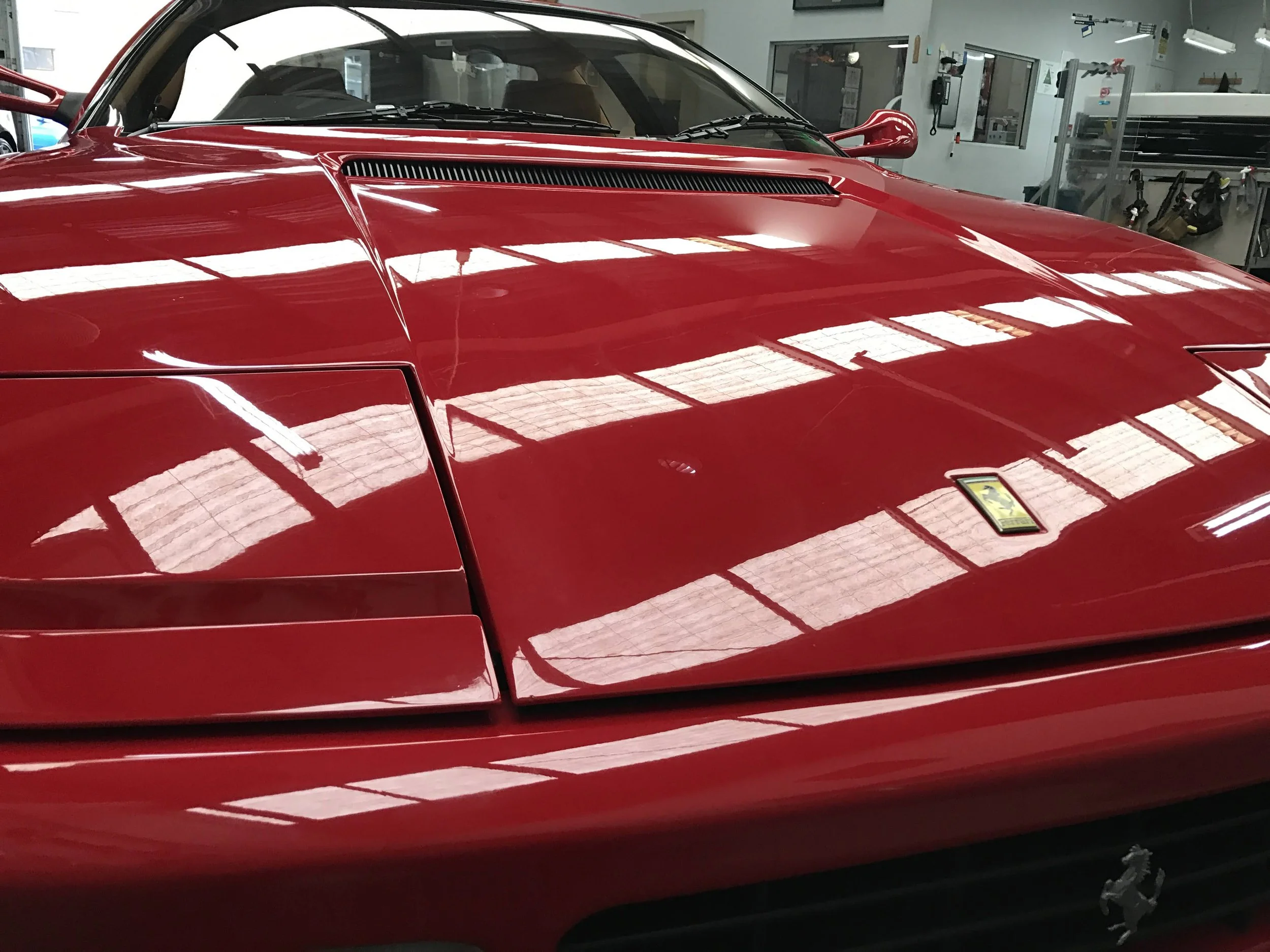 Close-up of a shiny red sports car parked inside a garage, reflecting the ceiling lights.