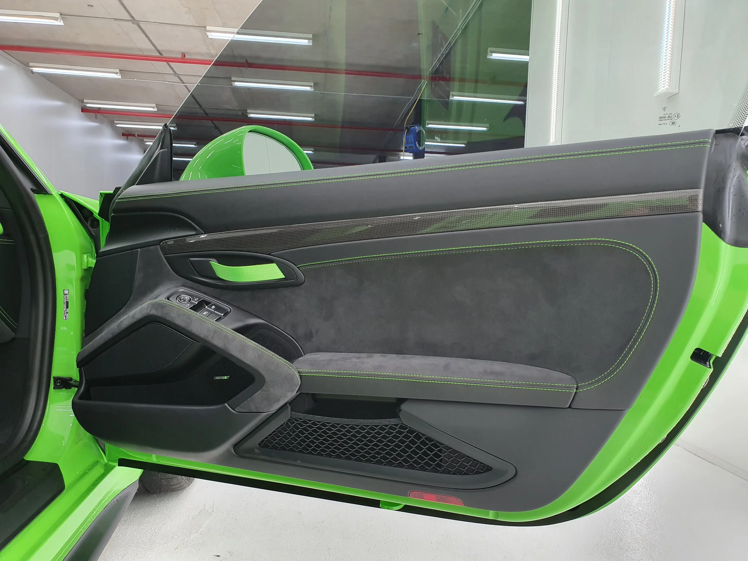 Close-up of the open driver's side door of a green sports car, showing black interior with green stitching, a handle, and speaker.