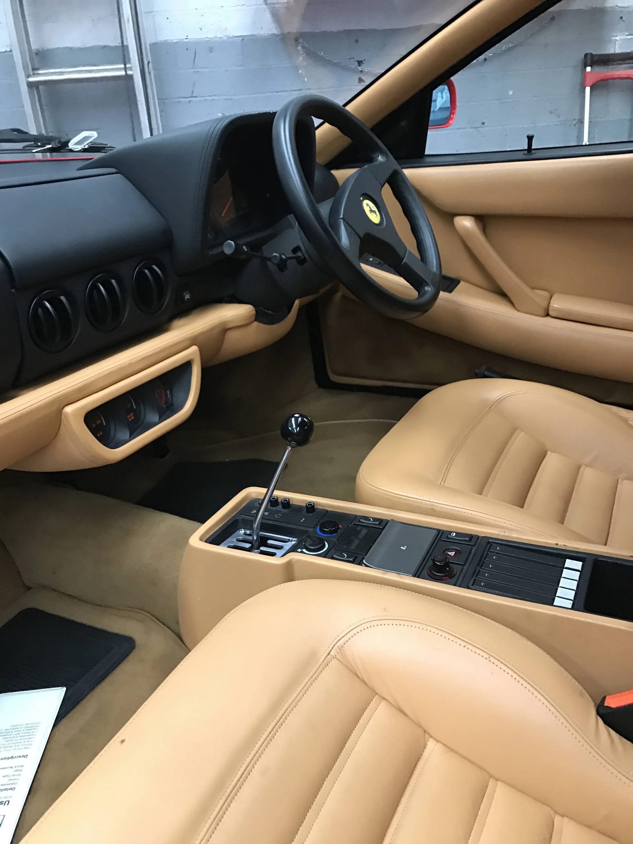 Interior of a classic sports car with tan leather seats, black dashboard, and a gear shift in the center console.