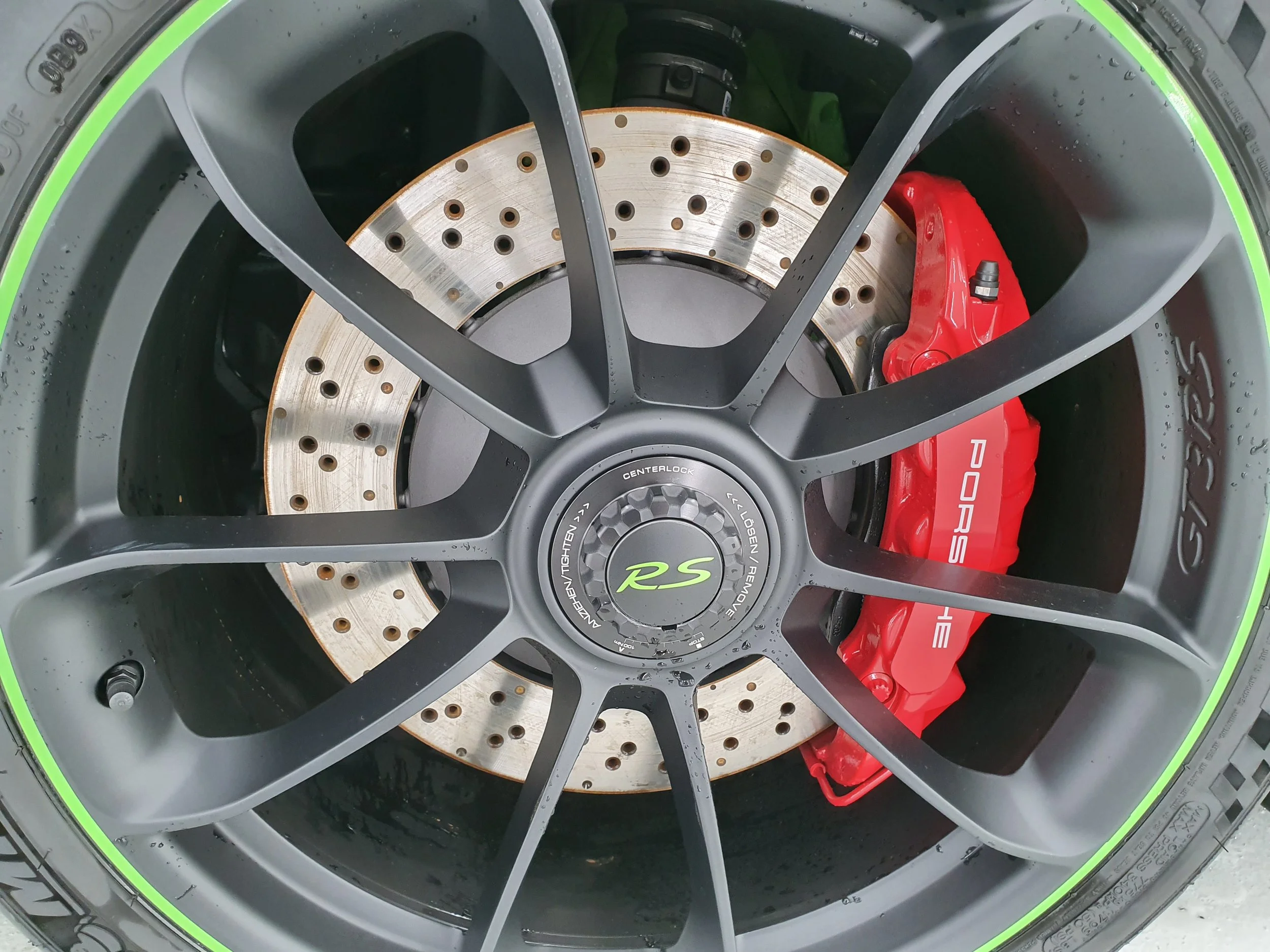 Close-up of a high-performance car brake system with a ventilated brake disc, a red brake caliper, and a black wheel rim with green accents.