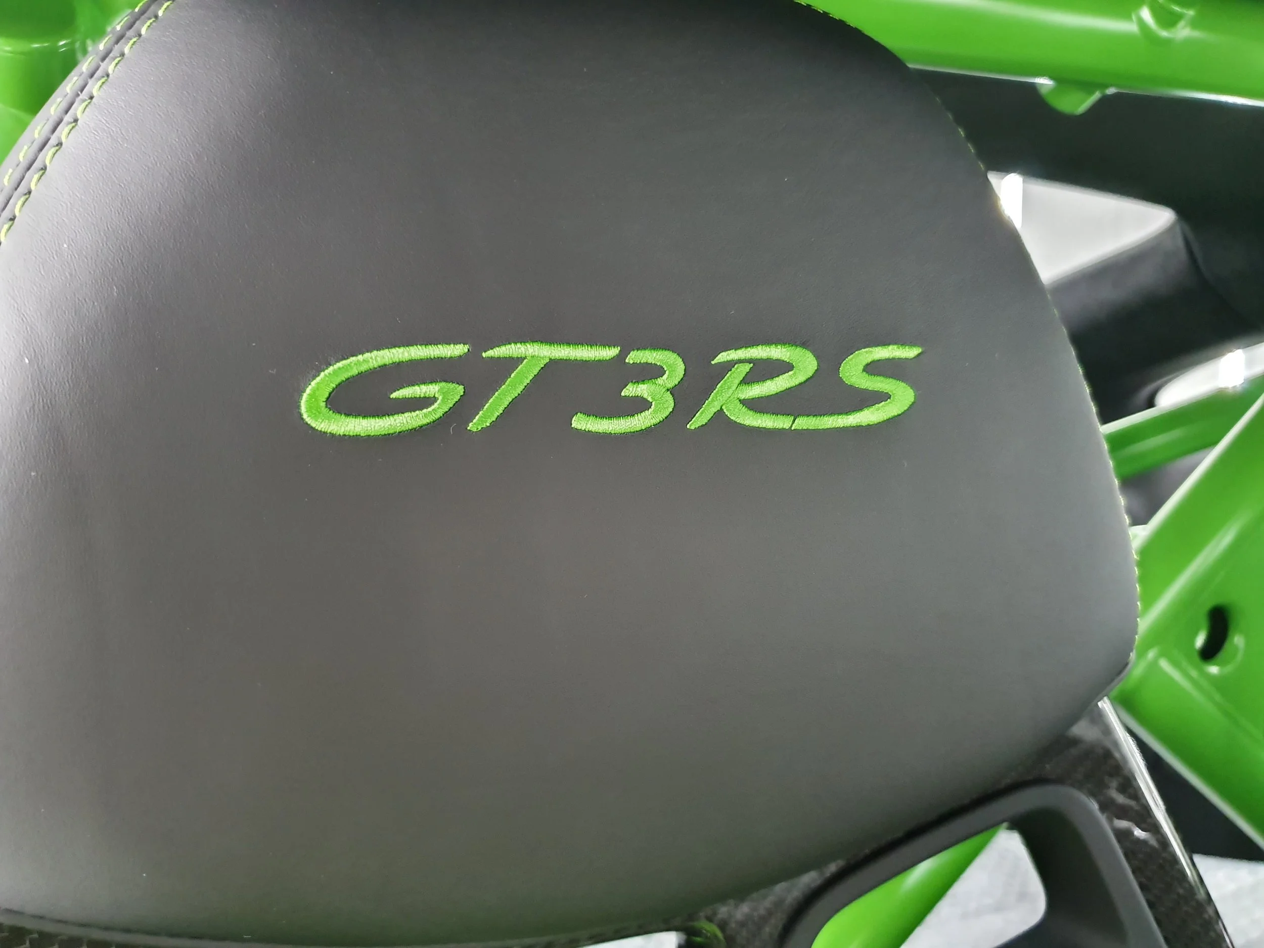 Close-up of a black surface with green embroidery reading GTR3RS, part of a green bicycle frame and wheel.