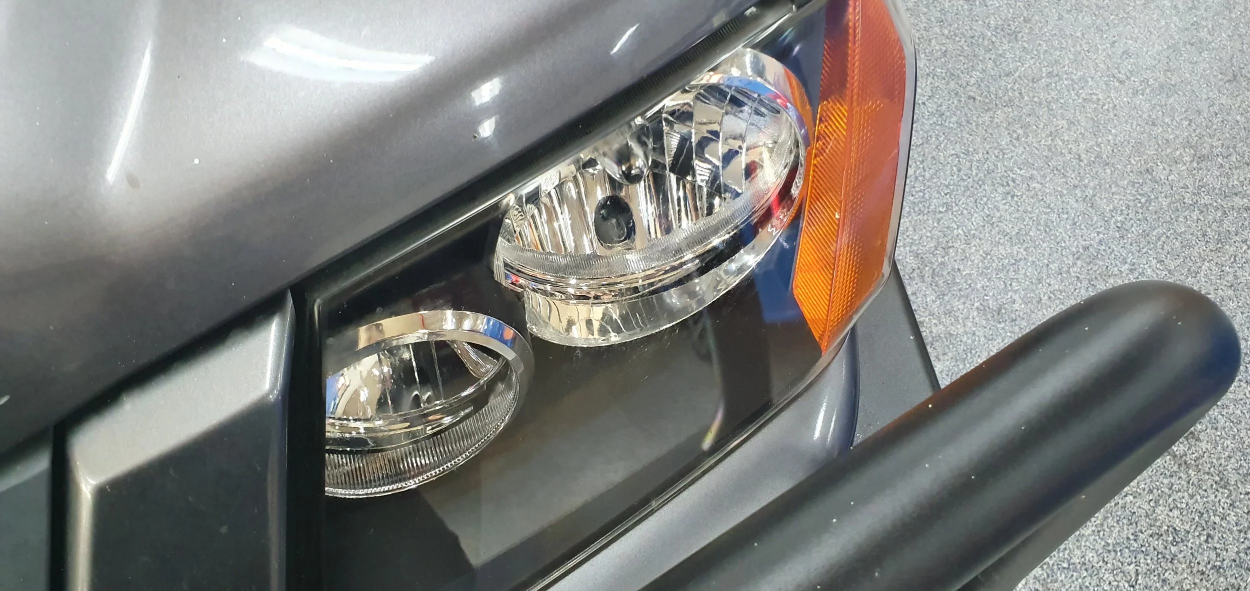 Close-up of a vehicle's front headlights, showing dual round lights with reflective surfaces and an orange turn signal indicator.