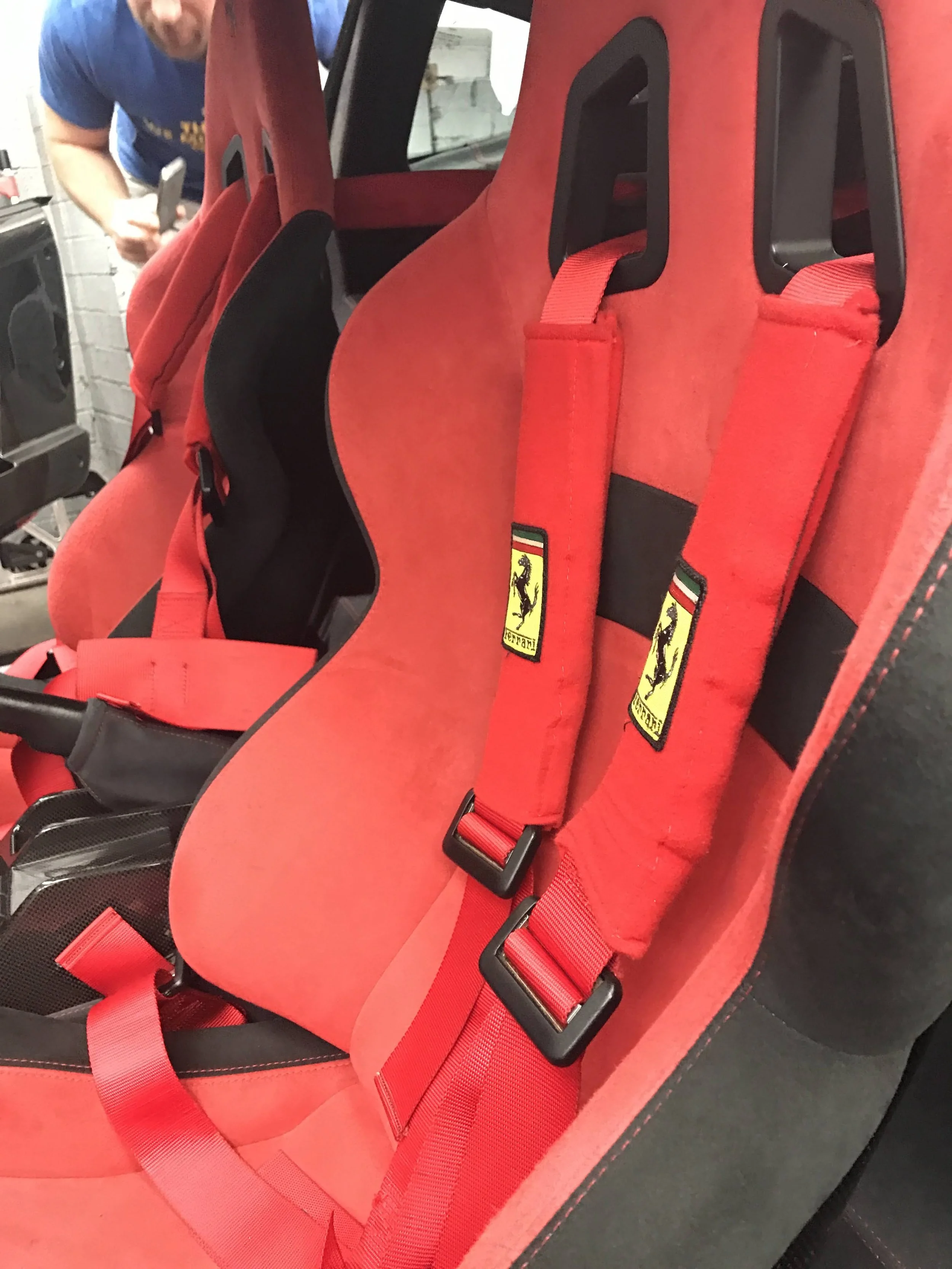 A close-up of three bright red racing car seats with black harness slots and the Ferrari logo below the slots, arranged in a row in a vehicle interior.