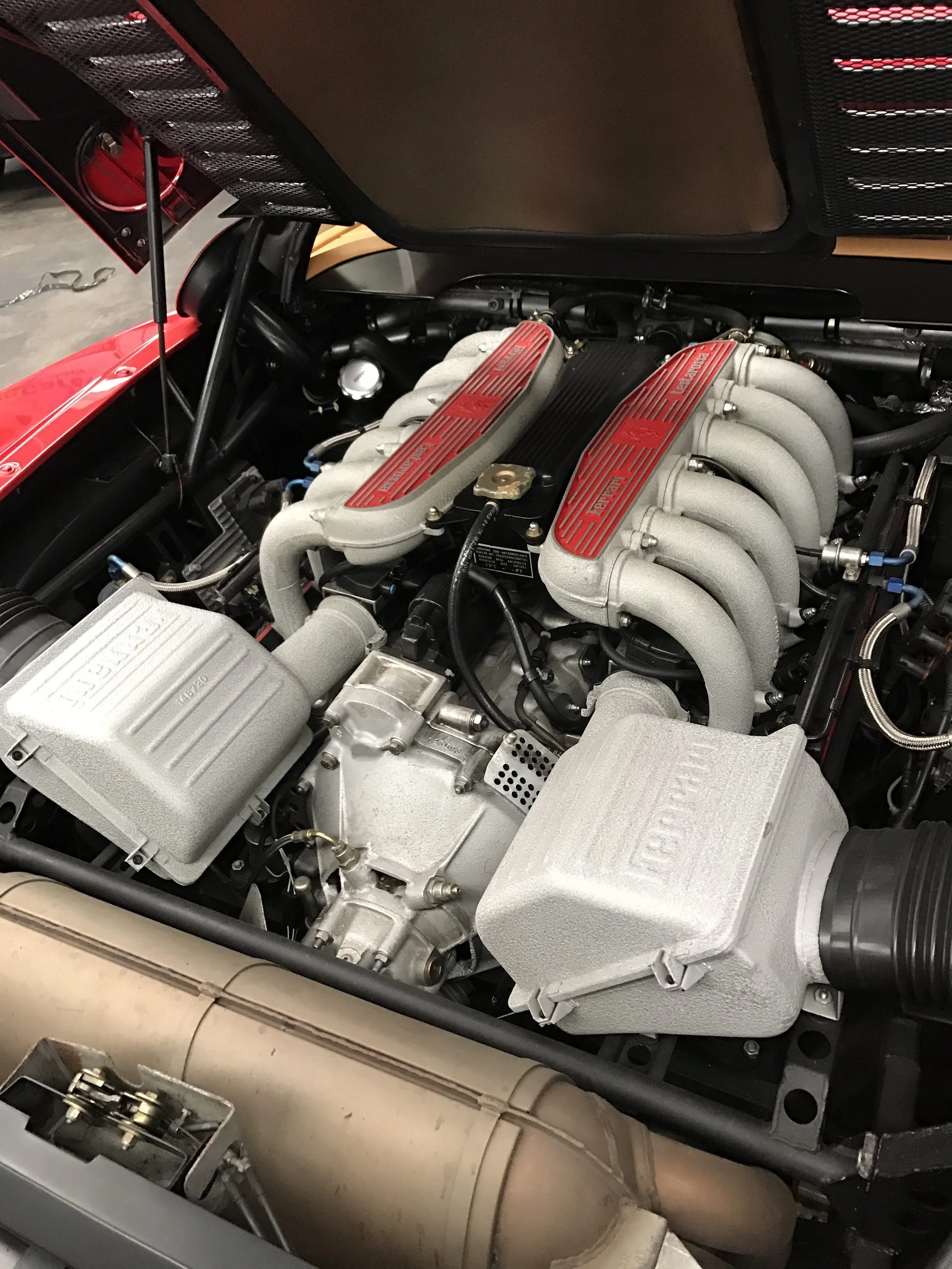 Close-up view of a car engine with red valve covers labeled 'Ferrari' and various mechanical components.