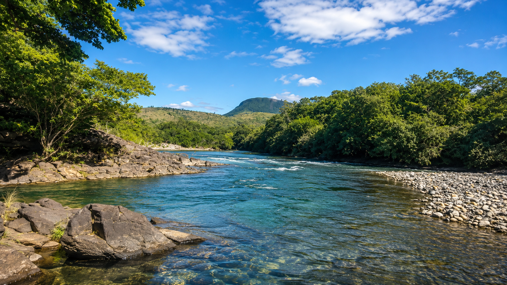 Une rivière bordée d'arbres verts et de galets dans un paysage naturel avec des montagnes en arrière-plan sous un ciel bleu avec quelques nuages.