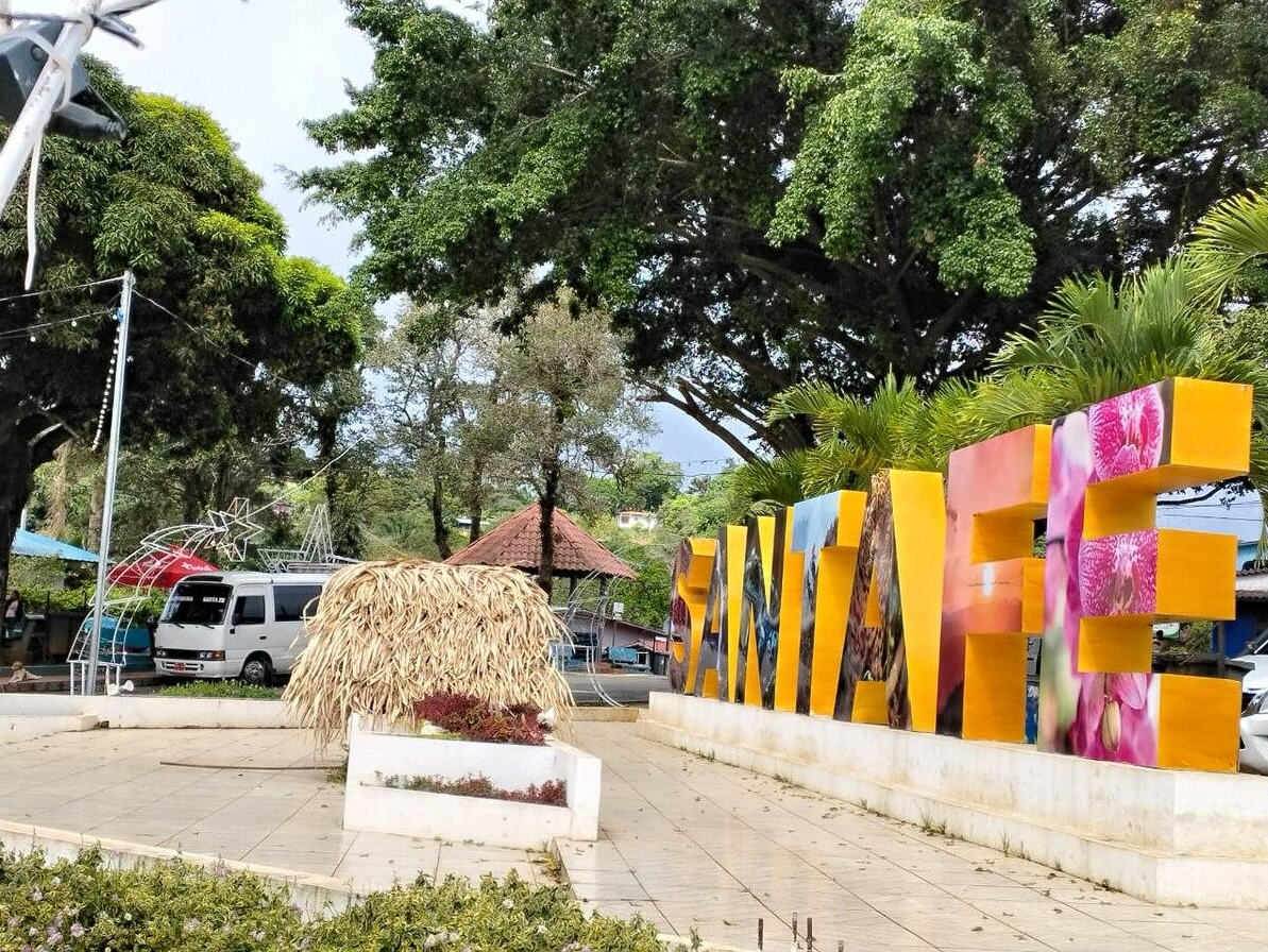 Une grande enseigne en lettres colorées indiquant « SANTA Eﬁ » située dans un espace public en plein air avec des arbres et des véhicules en arrière-plan.