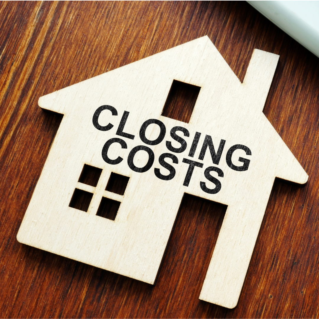 A wooden house-shaped cutout with the words 'Closing Costs' printed in black, lying on a wooden surface.