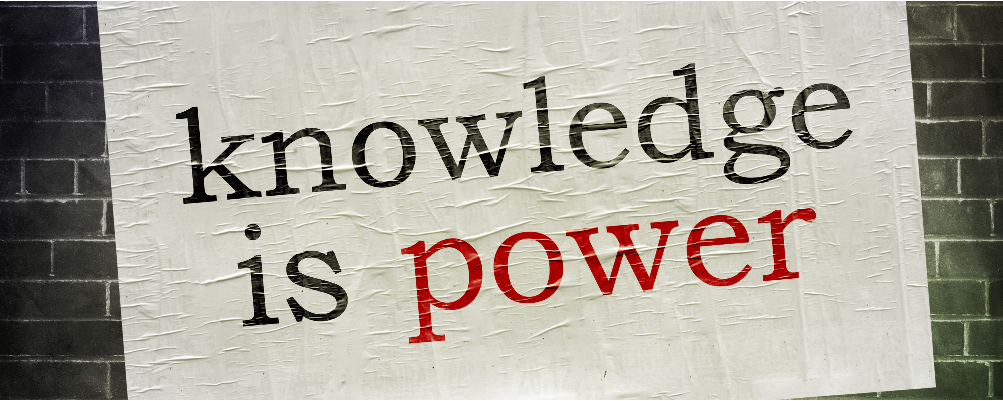 A sign with the words 'knowledge is power' printed, with 'knowledge' and 'is' in black lowercase letters and 'power' in bold red letters, mounted on a brick wall.