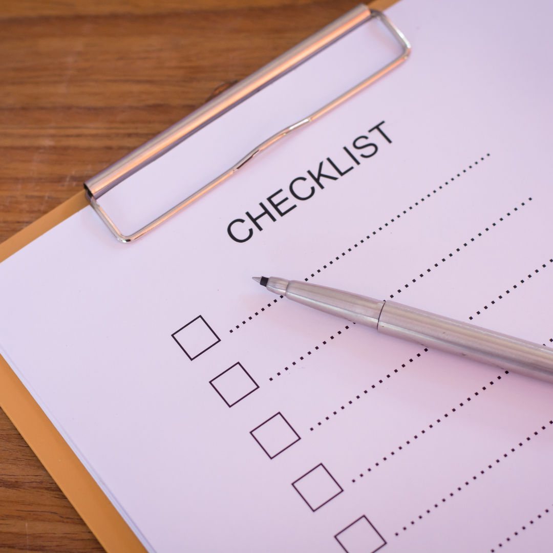 A checklist on a clipboard with empty checkboxes, a silver pen, on a wooden surface.