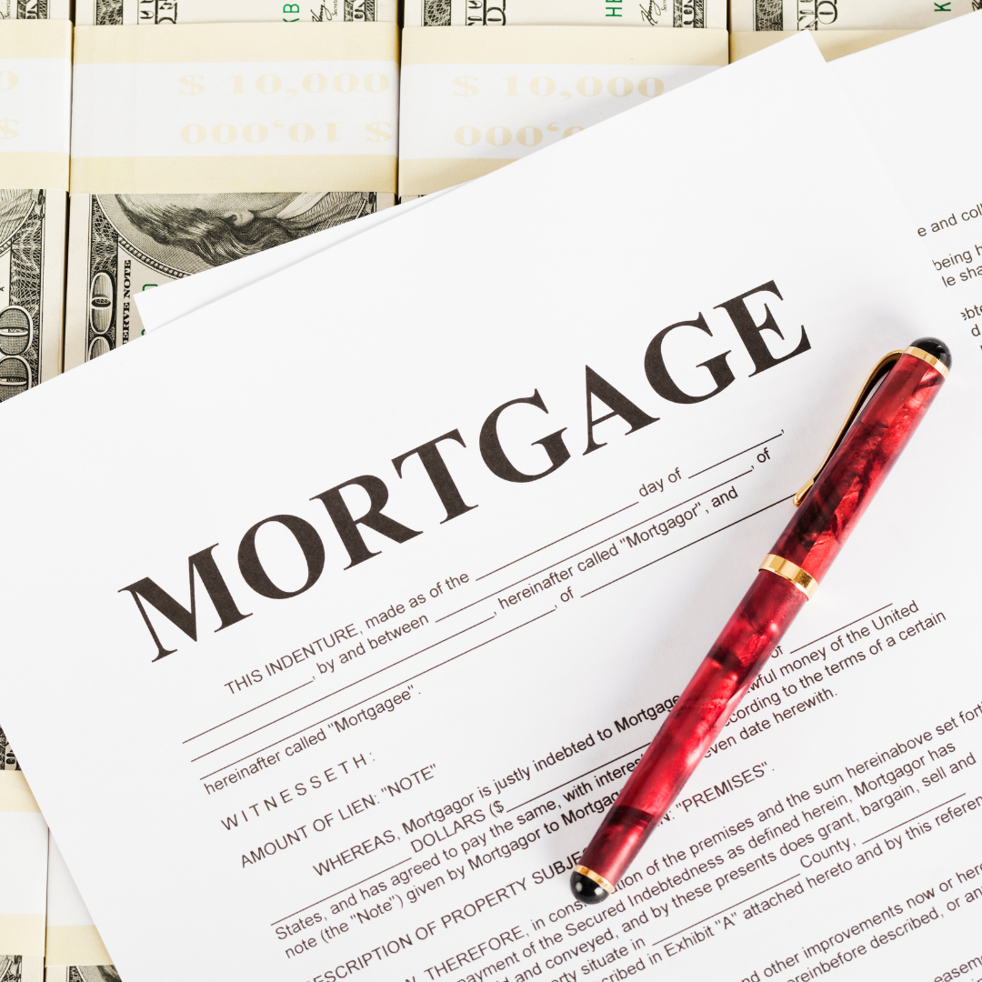 A mortgage document with a red and gold capped pen resting on top, surrounded by several bundles of hundred-dollar bills.