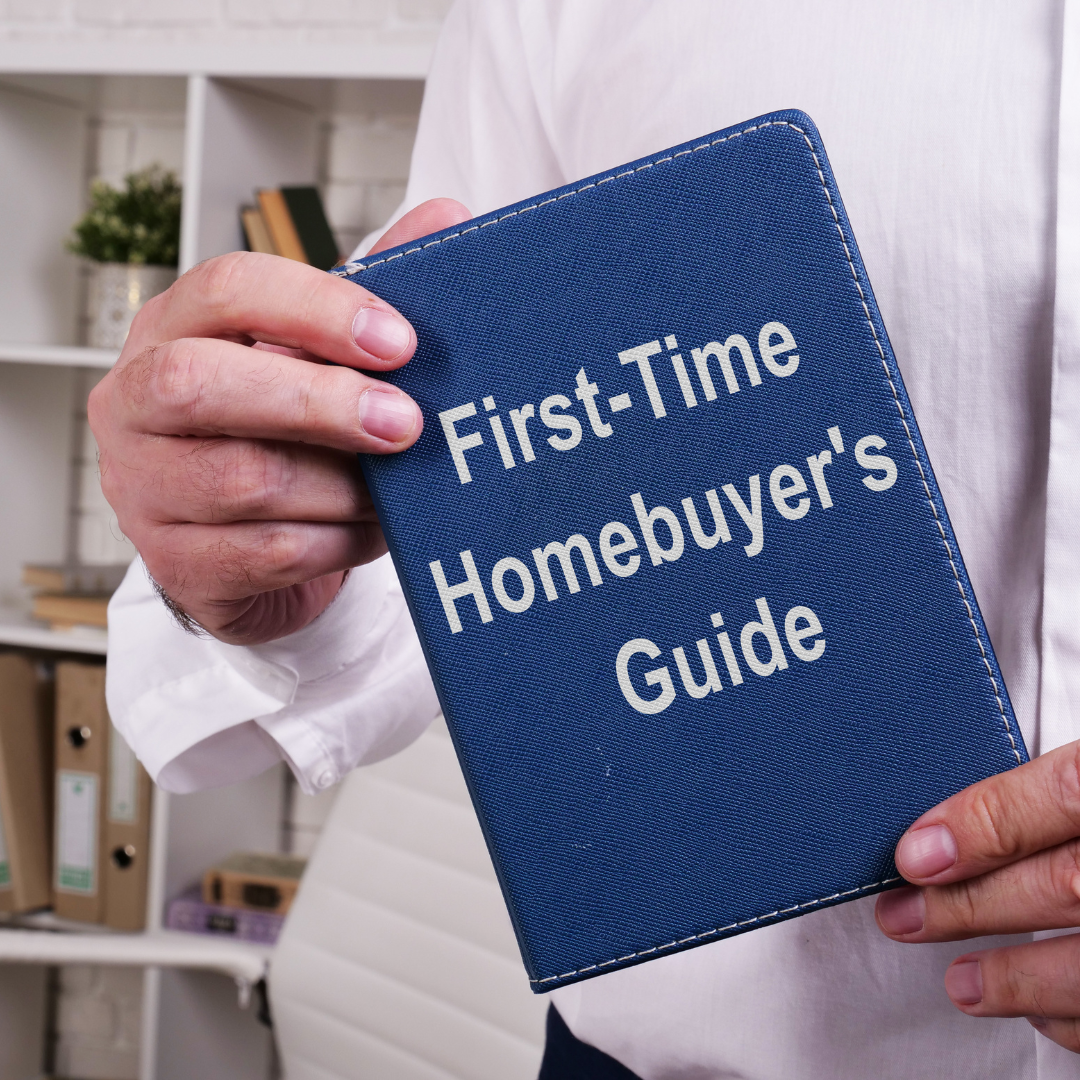 Person holding a blue guidebook titled 'First-Time Homebuyer's Guide' in an office setting.