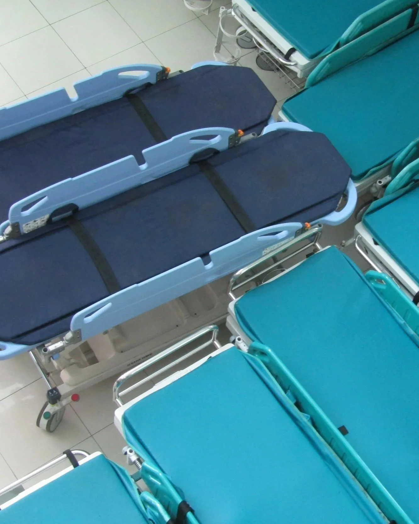 Hospital rooms with two empty blue medical stretchers and four teal-colored chairs.
