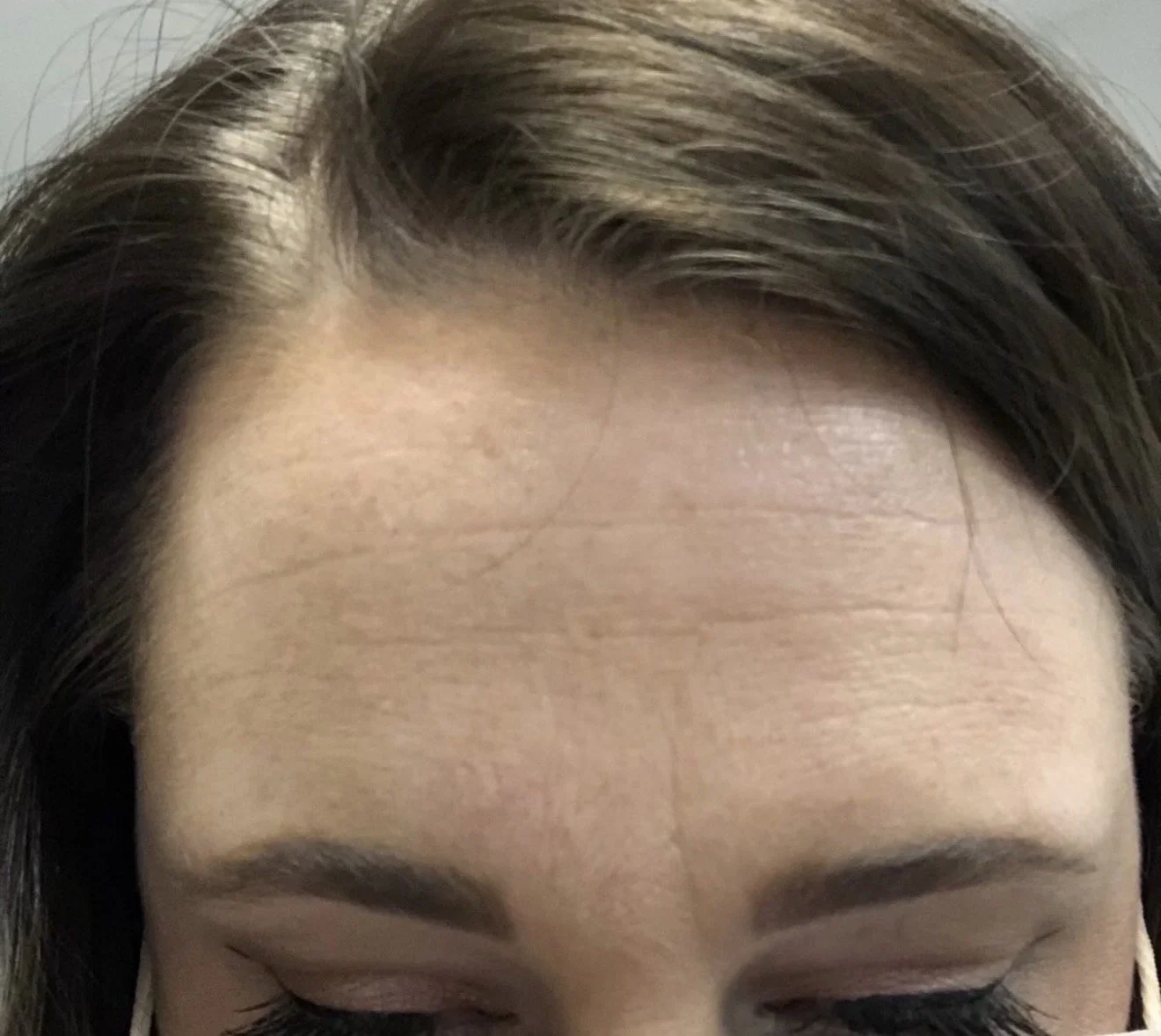 Close-up of a woman's forehead, with dark eyebrows and partially visible closed eyes, showing smooth skin and hair styled to the side.