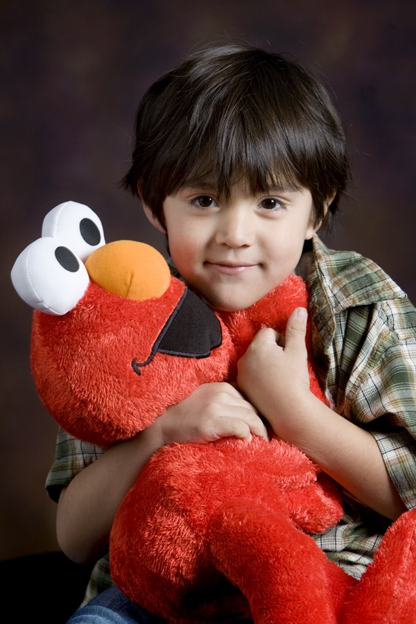 A young boy holding a large red Elmo plush toy from Sesame Street, smiling at the camera.