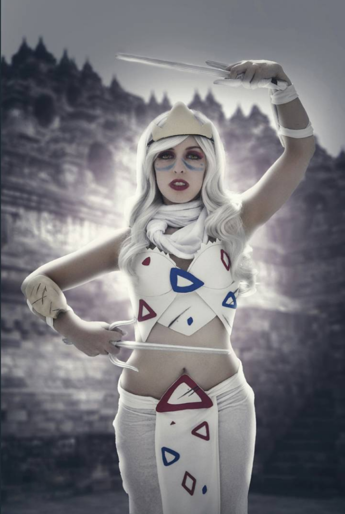 A person dressed as togepi with a white wig, face makeup, and a crown, holding a wand in front of a snowy landscape with pine trees.