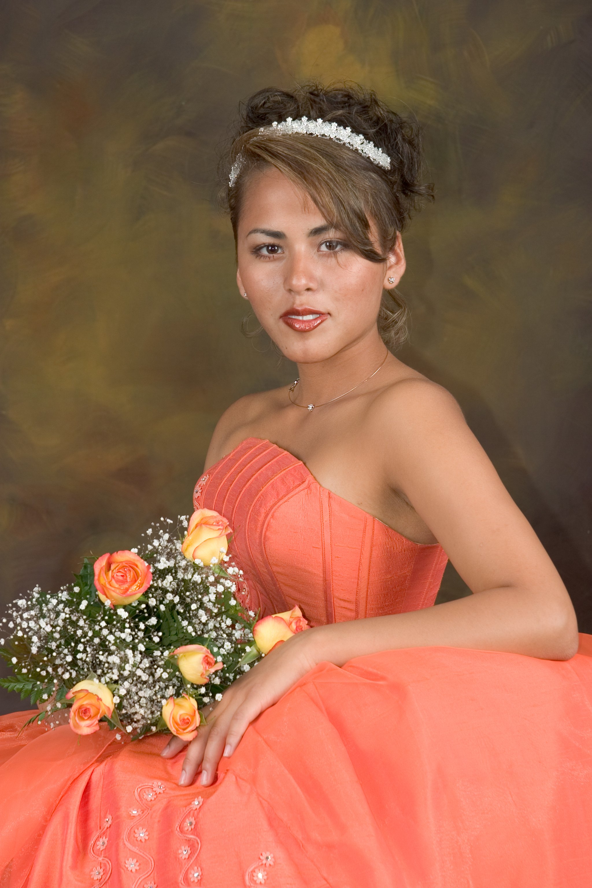 Young woman wearing an orange strapless dress and a tiara, holding a bouquet of orange roses and white flowers, with a textured, abstract background.