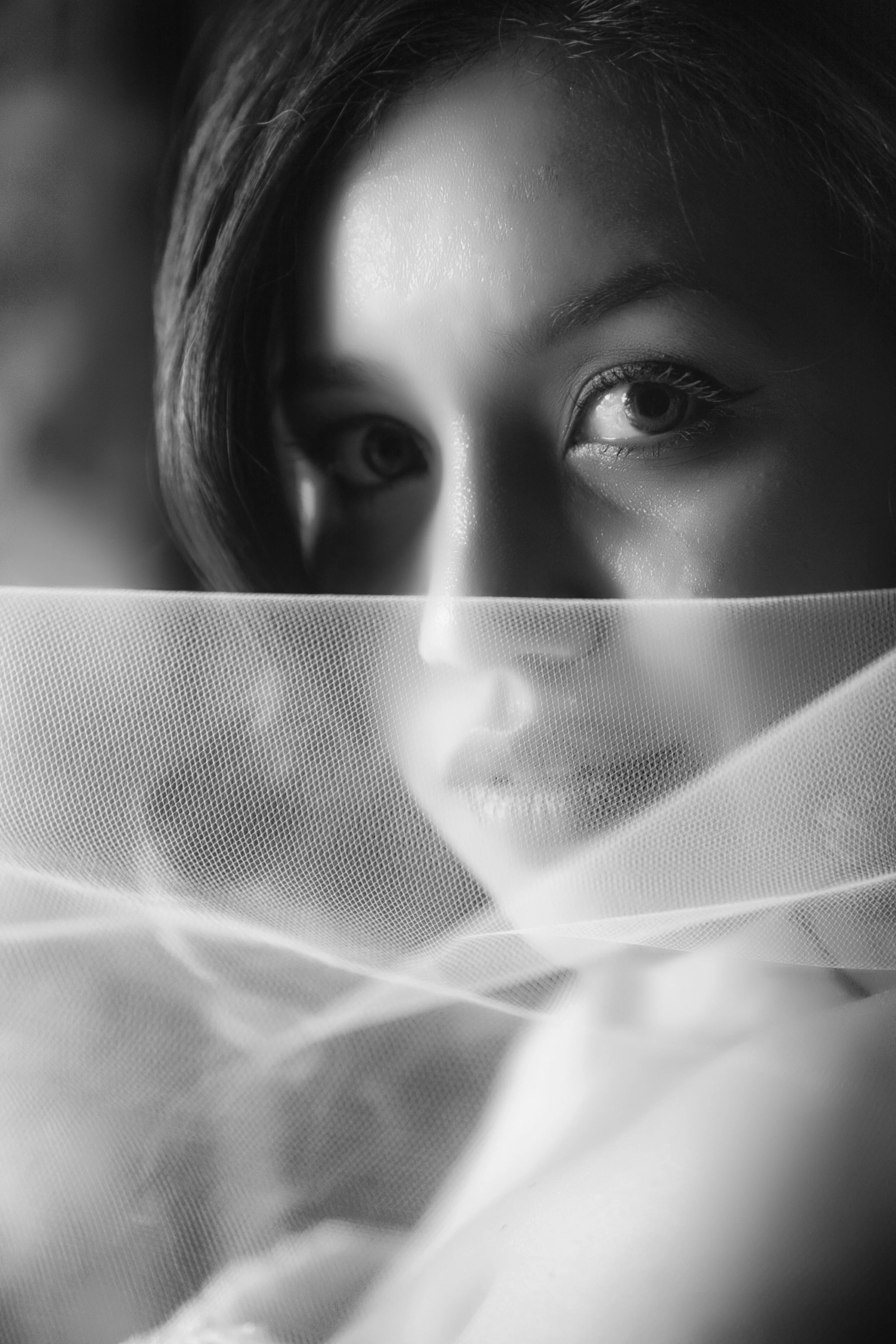 Close-up of a woman's face with focus on her eyes, partially obscured by sheer fabric.