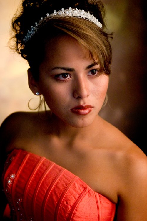 Young woman with light skin wearing a tiara, earrings, and a red strapless dress.