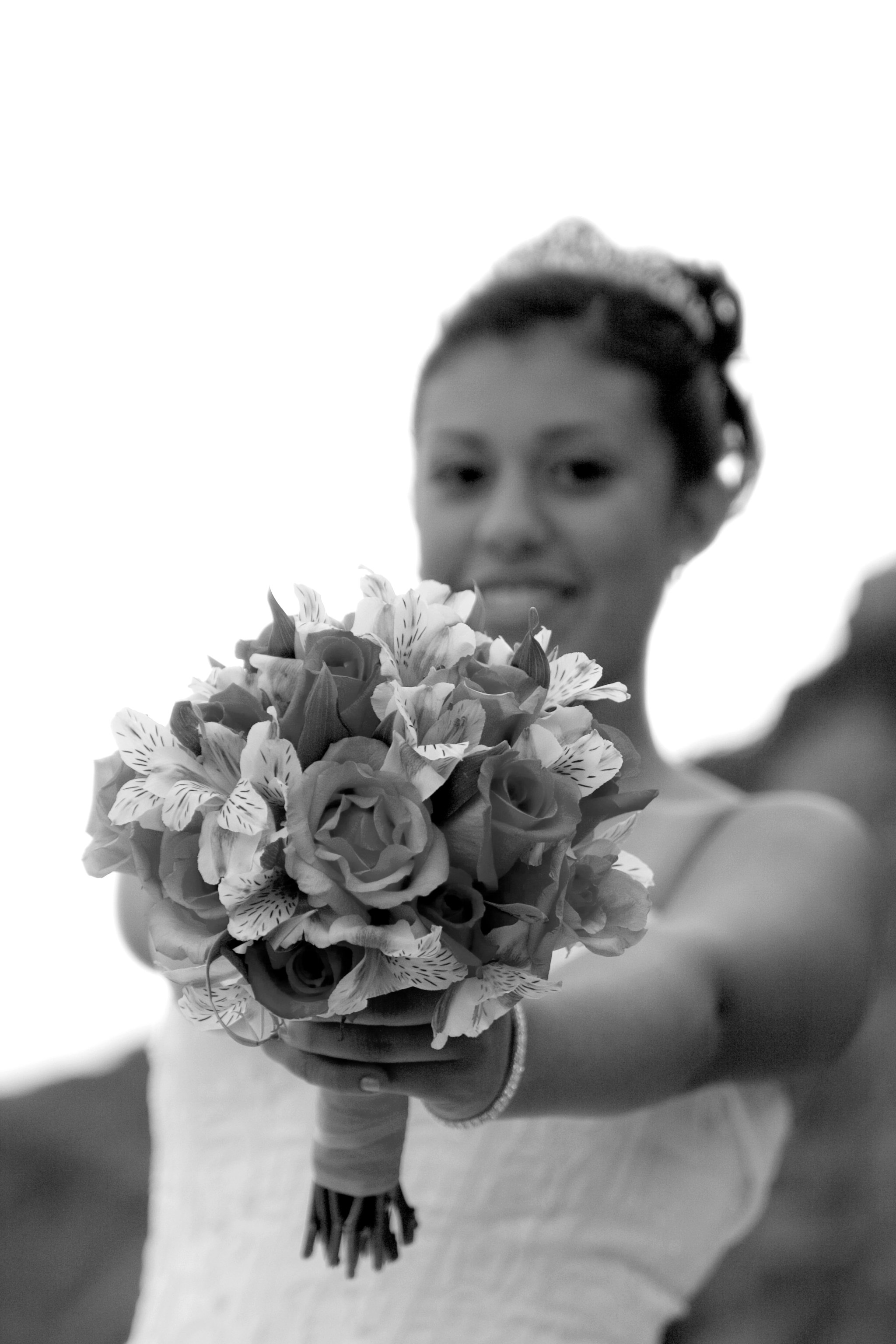 A woman holding a bouquet of flowers in front of her face, with only the top of her head and her eyes visible, in a black and white photo.