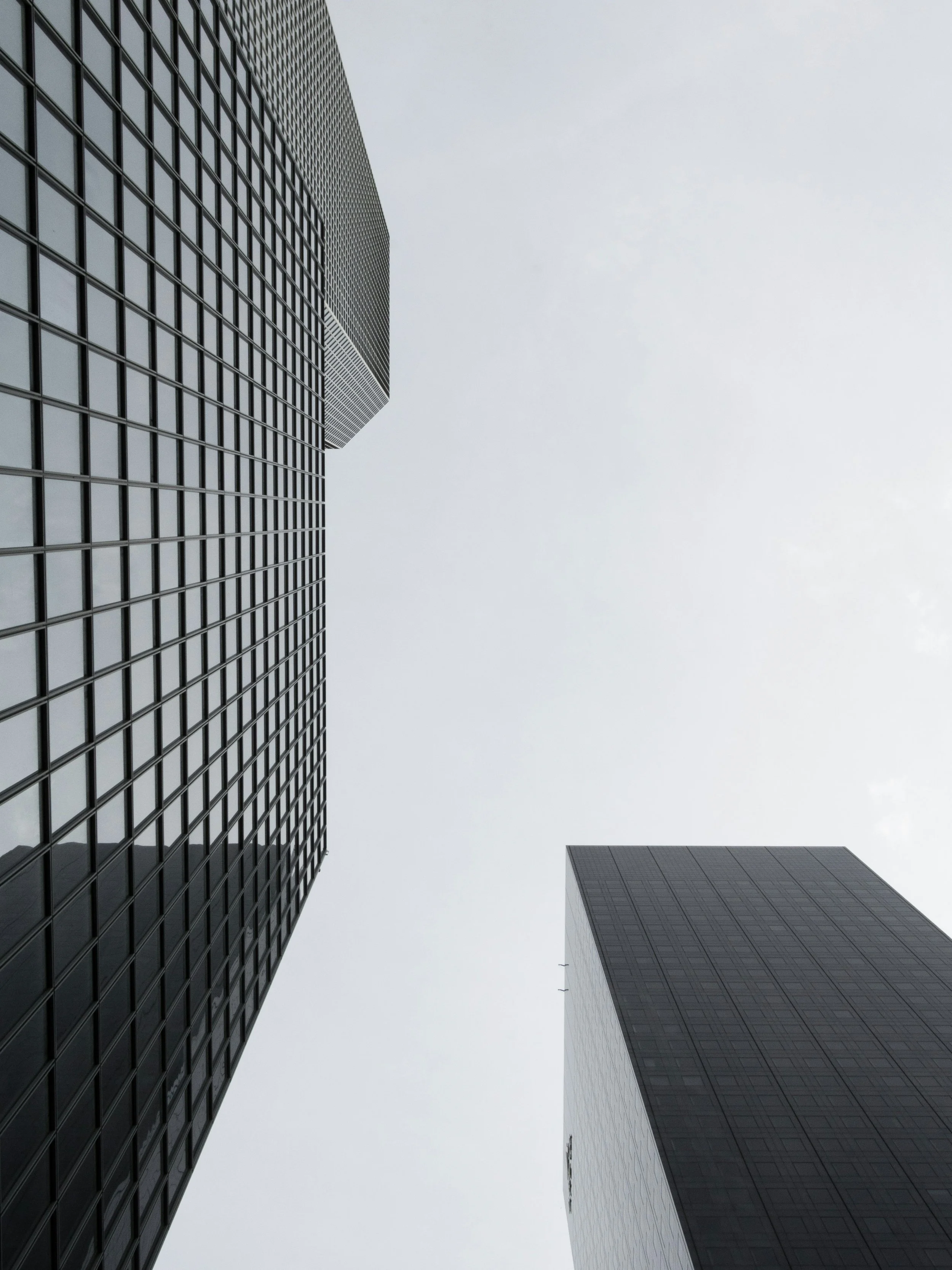 Low-angle view of tall modern skyscrapers with glass facades against a cloudy sky.