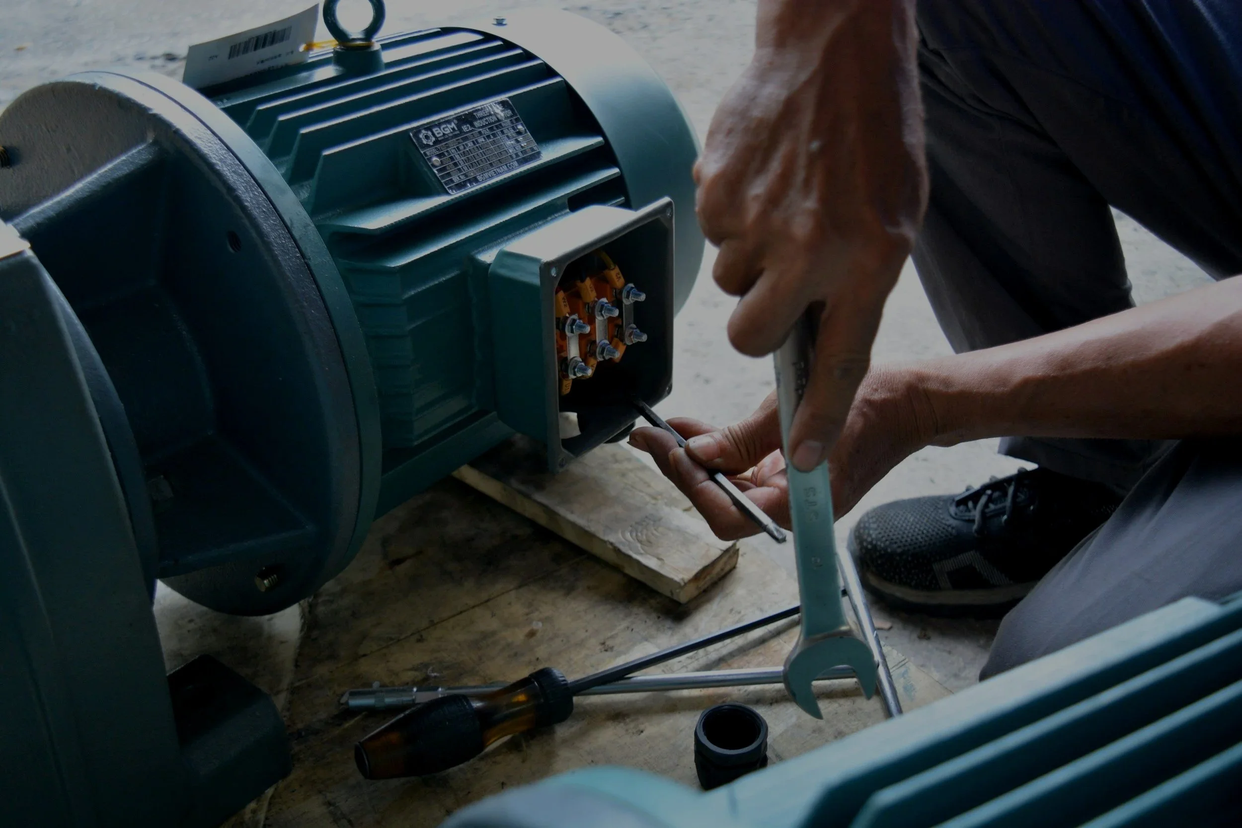 A person working on an electric motor, using a screwdriver, with tools and parts nearby.