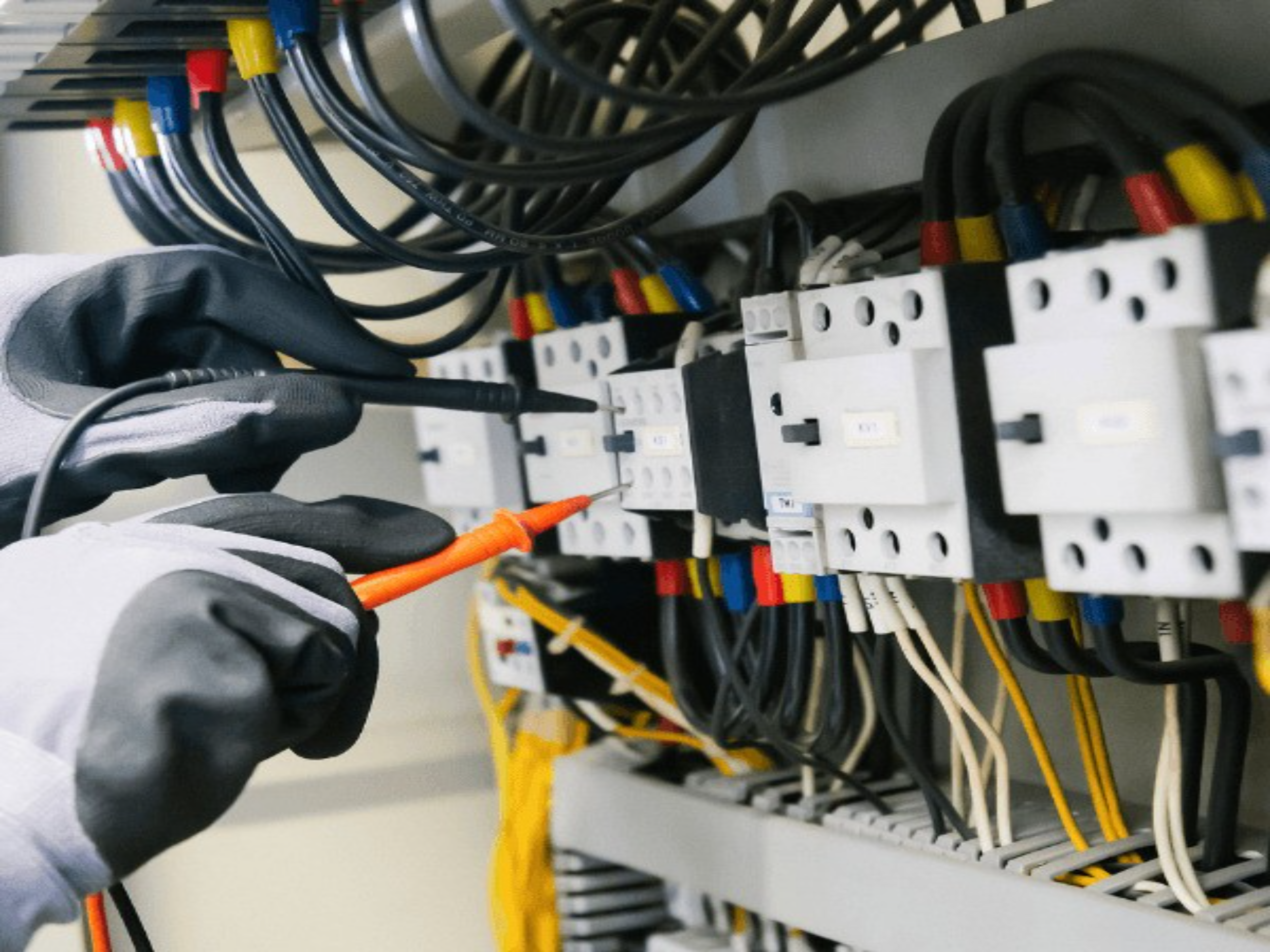 Person wearing gray and black gloves working on a network or electrical panel with numerous black, yellow, red, blue, and white wires and connectors.