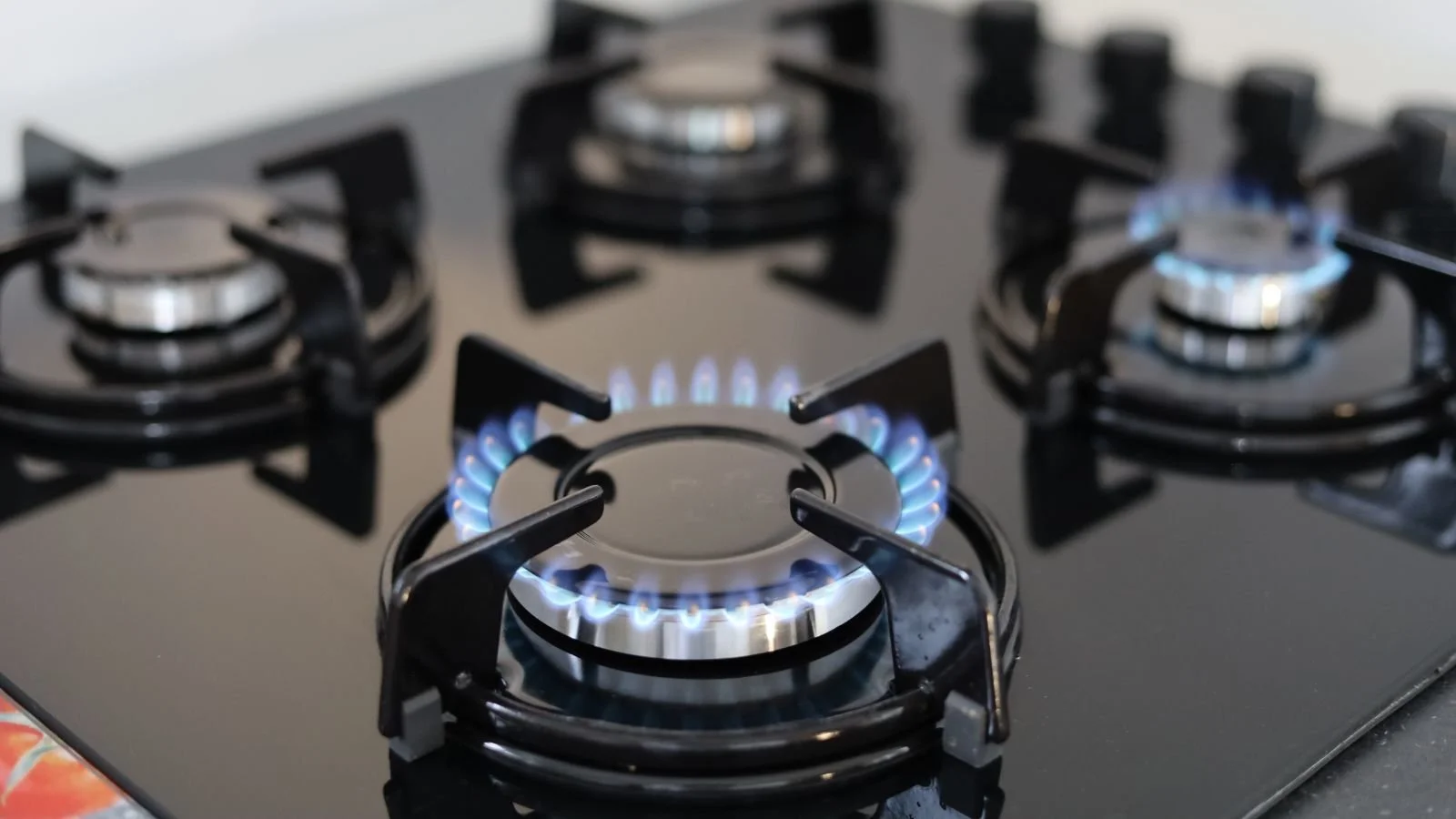 Close-up of a black gas stove with three lit burners showing blue flames.