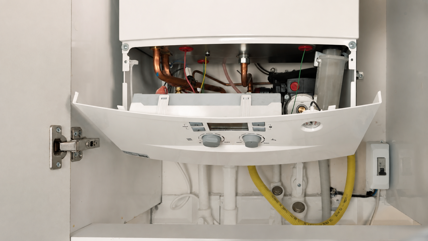 Open cabinet with a water heater showing internal copper pipes, wiring, and control knobs.