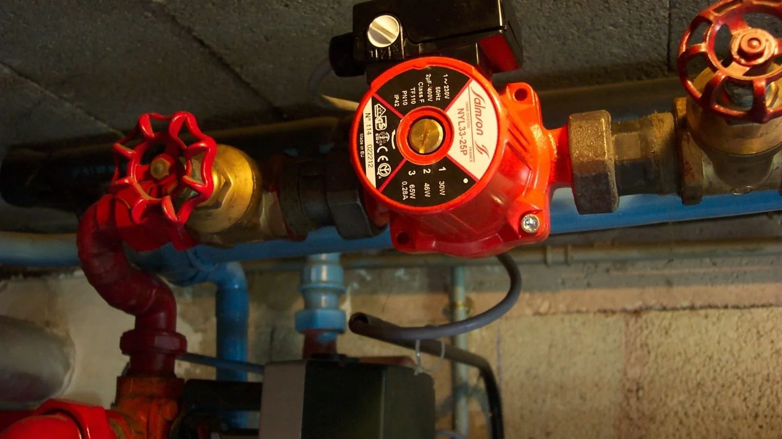 Close-up view of a red circs control valve attached to pipes with a black control module nearby, in a mechanical room.