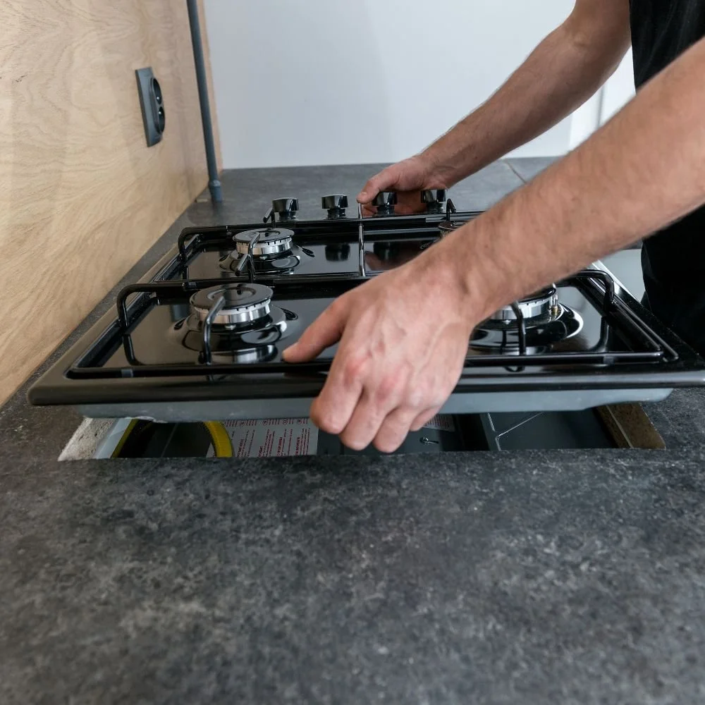 Person installing or adjusting a black gas stove with two burners in a kitchen.