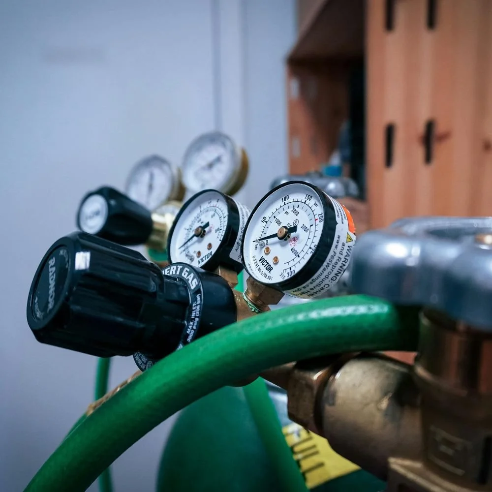 Close-up view of a gas cylinder regulator with pressure gauges and a green hose.