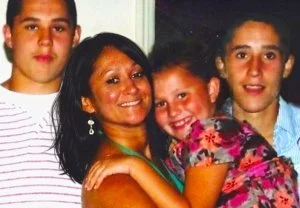 A woman with three children smiling and hugging in a close group.