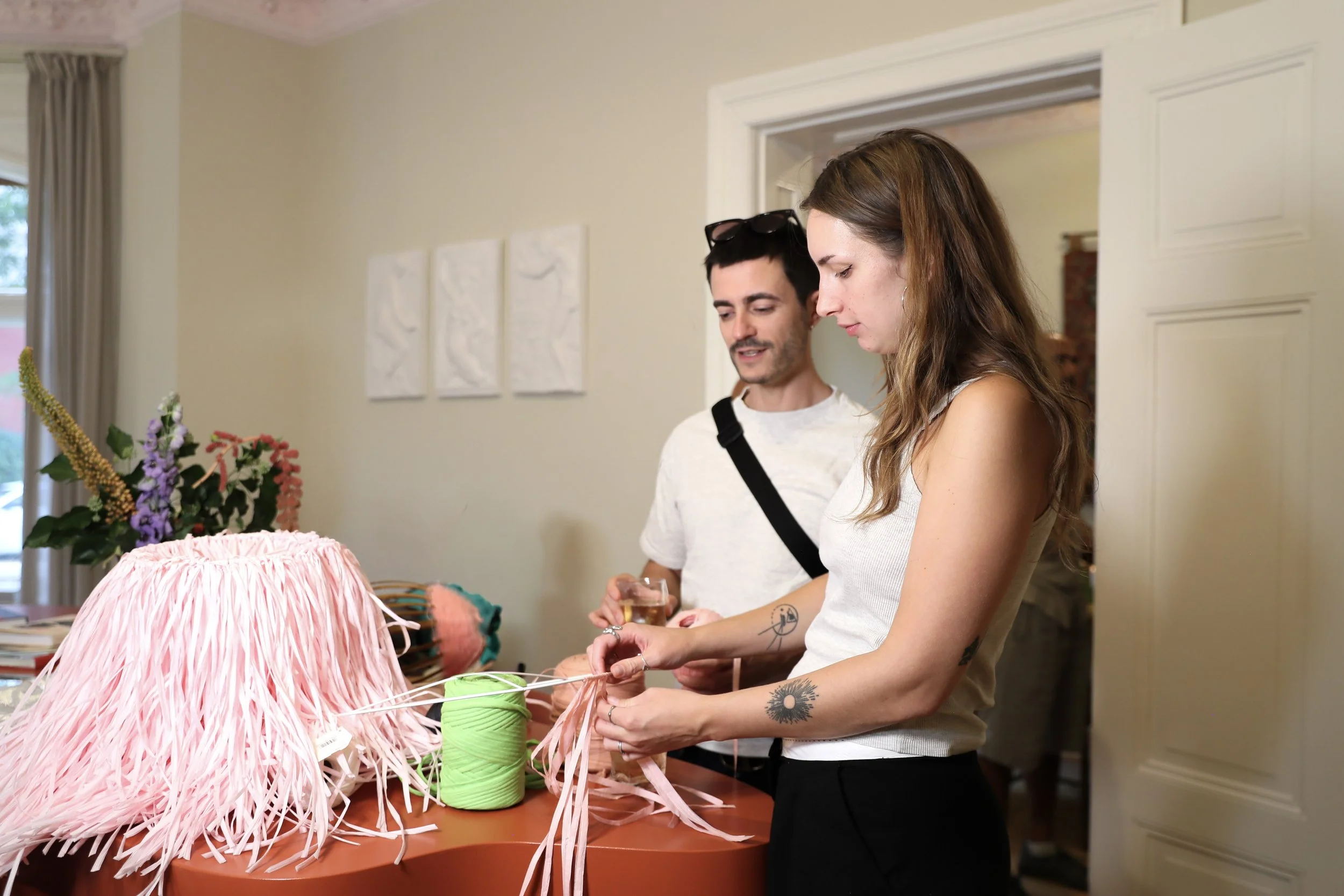Zwei Menschen, ein Mann und eine Frau, beim Basteln mit rosa Papier in einem Wohnzimmer.