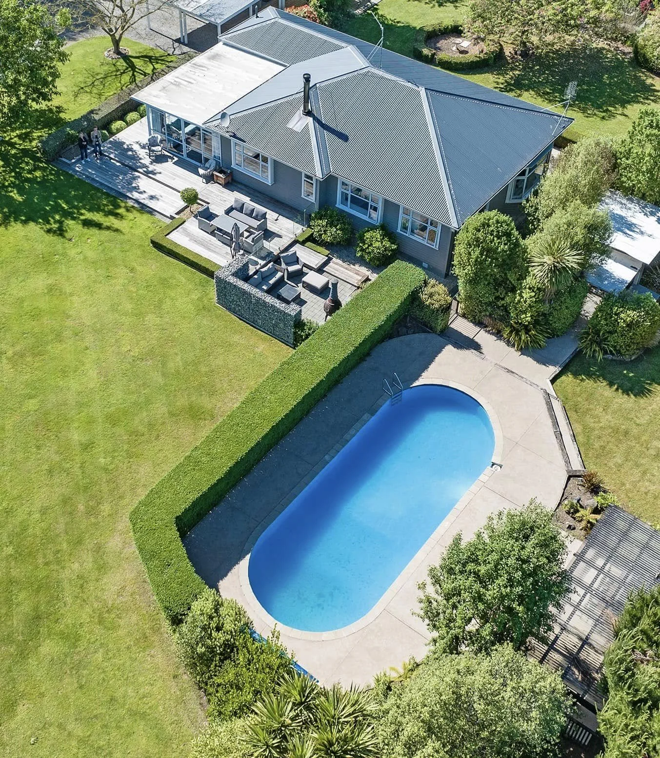 Aerial view of a house with a backyard, swimming pool, patio furniture, and landscaped yard with bushes, trees, and a lawn.