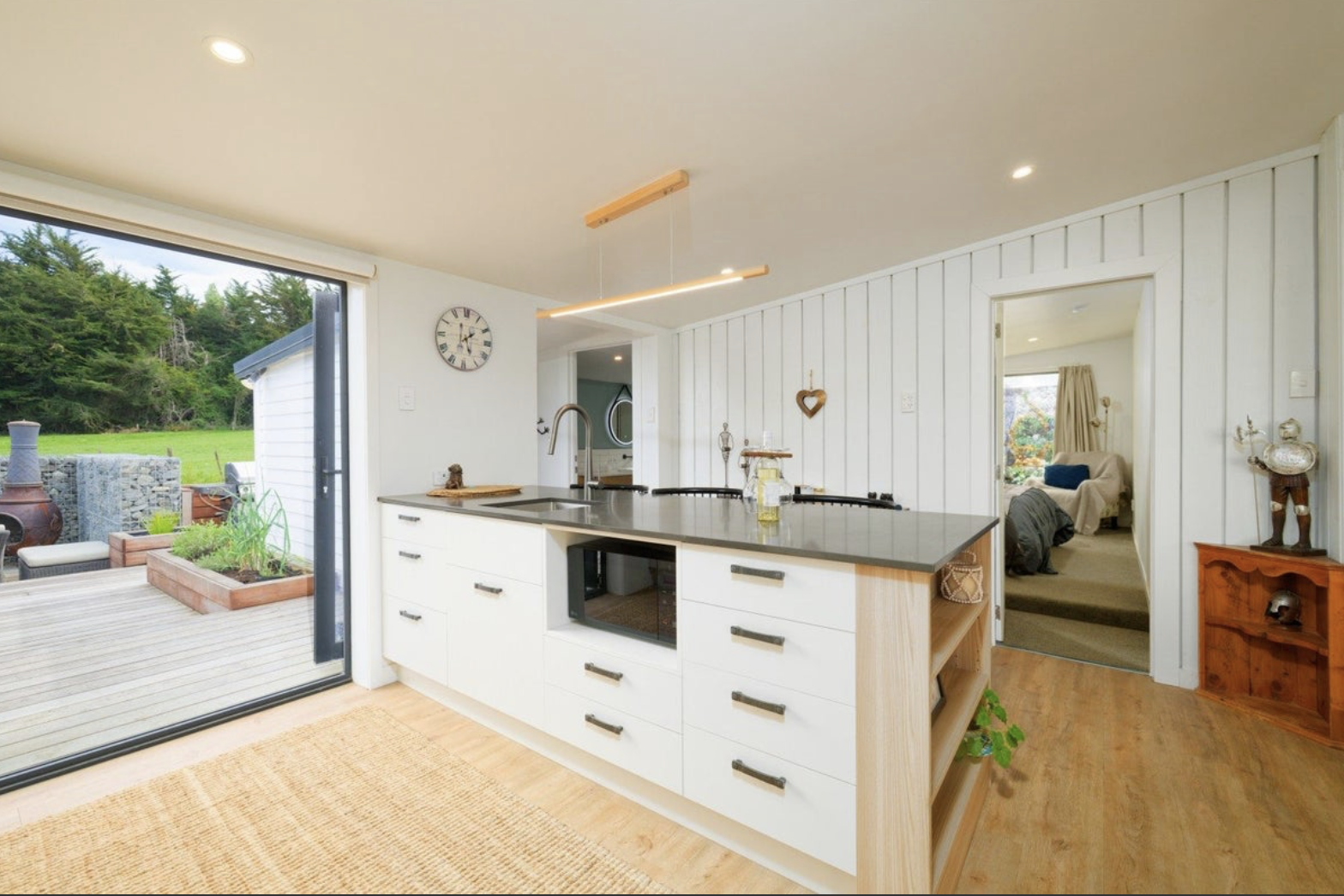 Modern kitchen with white cabinetry, black countertops, and a view of the outdoor patio and garden.