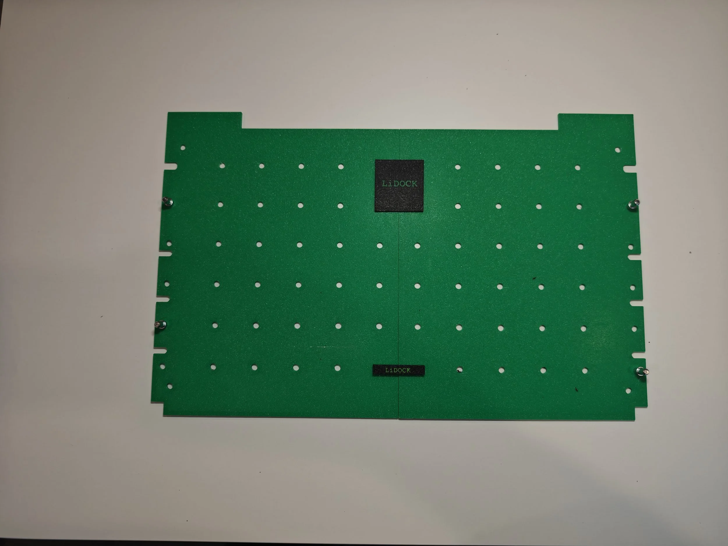 Green perforated metal plate with a central black label reading "LIDOCK" and smaller black label below also reading "LIDOCK," placed on a white surface.