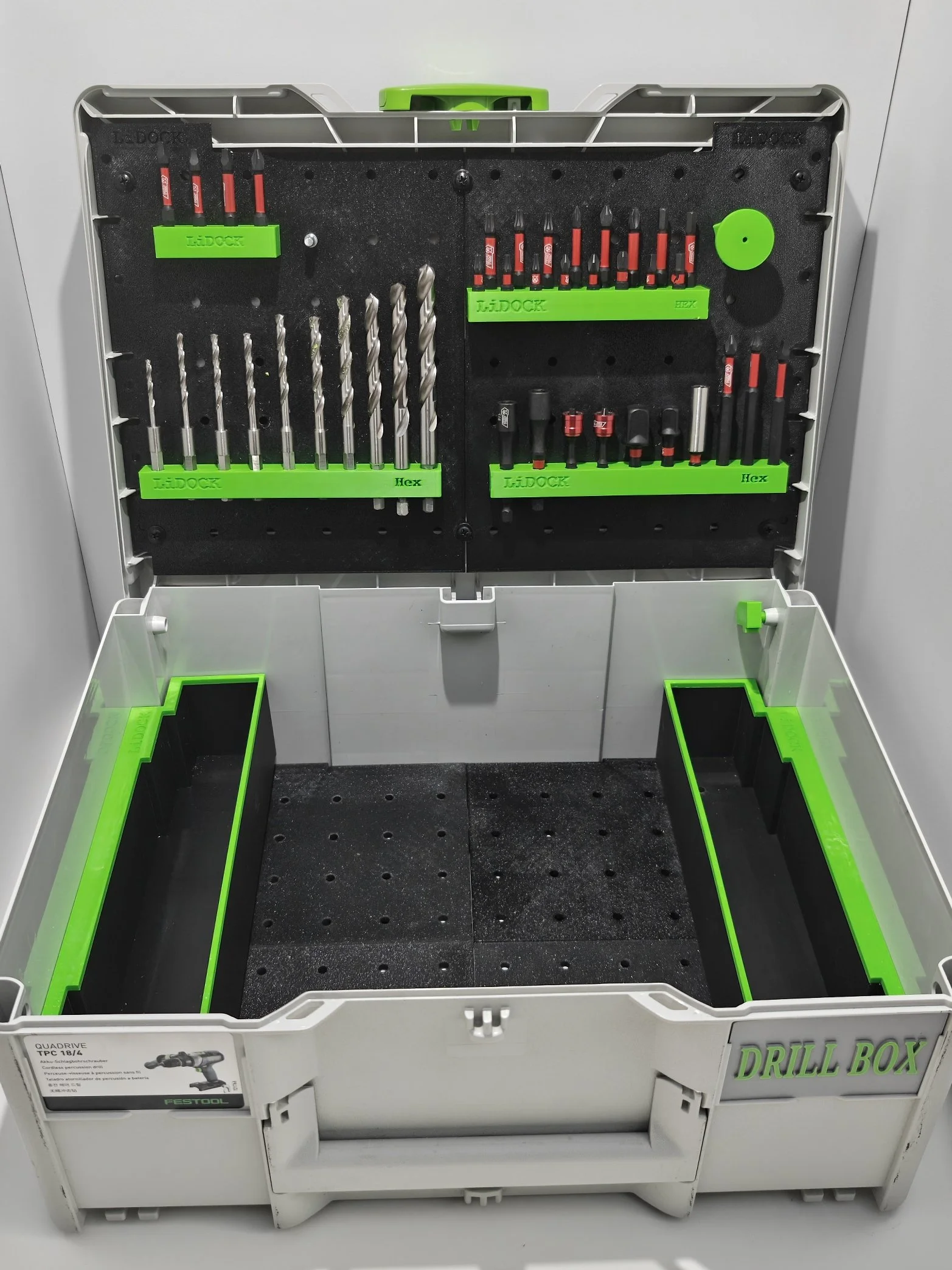 Open white plastic drill storage box with black foam interior and various drill bits organized in green labeled slots and spots, with the words "DRILL BOX" on the side.
