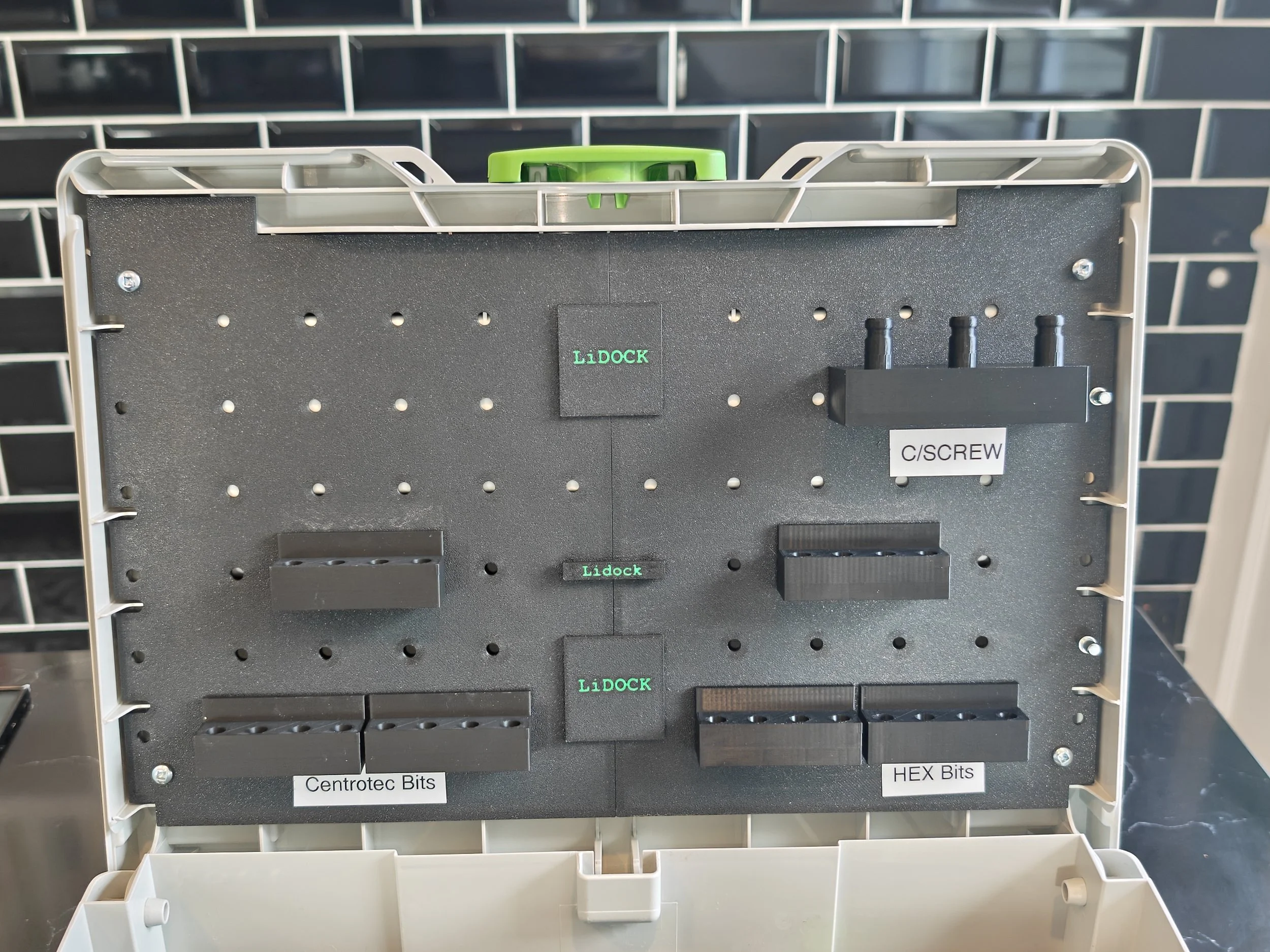 View of a pegboard with labeled sections for cassette tape bits, including 'Centrotec Bits,' 'LiDock,' and 'HEX Bits,' with a black metallic panel and green latches at the top.