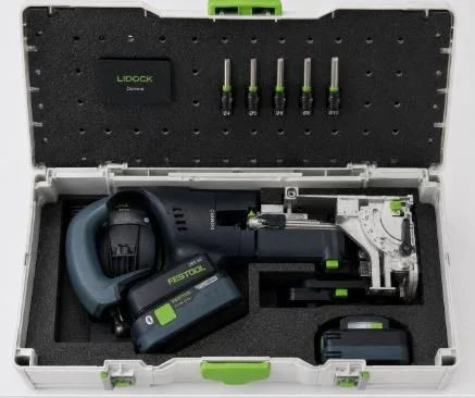 A power tool set in a gray and black carrying case with green accents, including a pneumatic nail gun, a battery pack, multiple drill bits, and associated accessories.