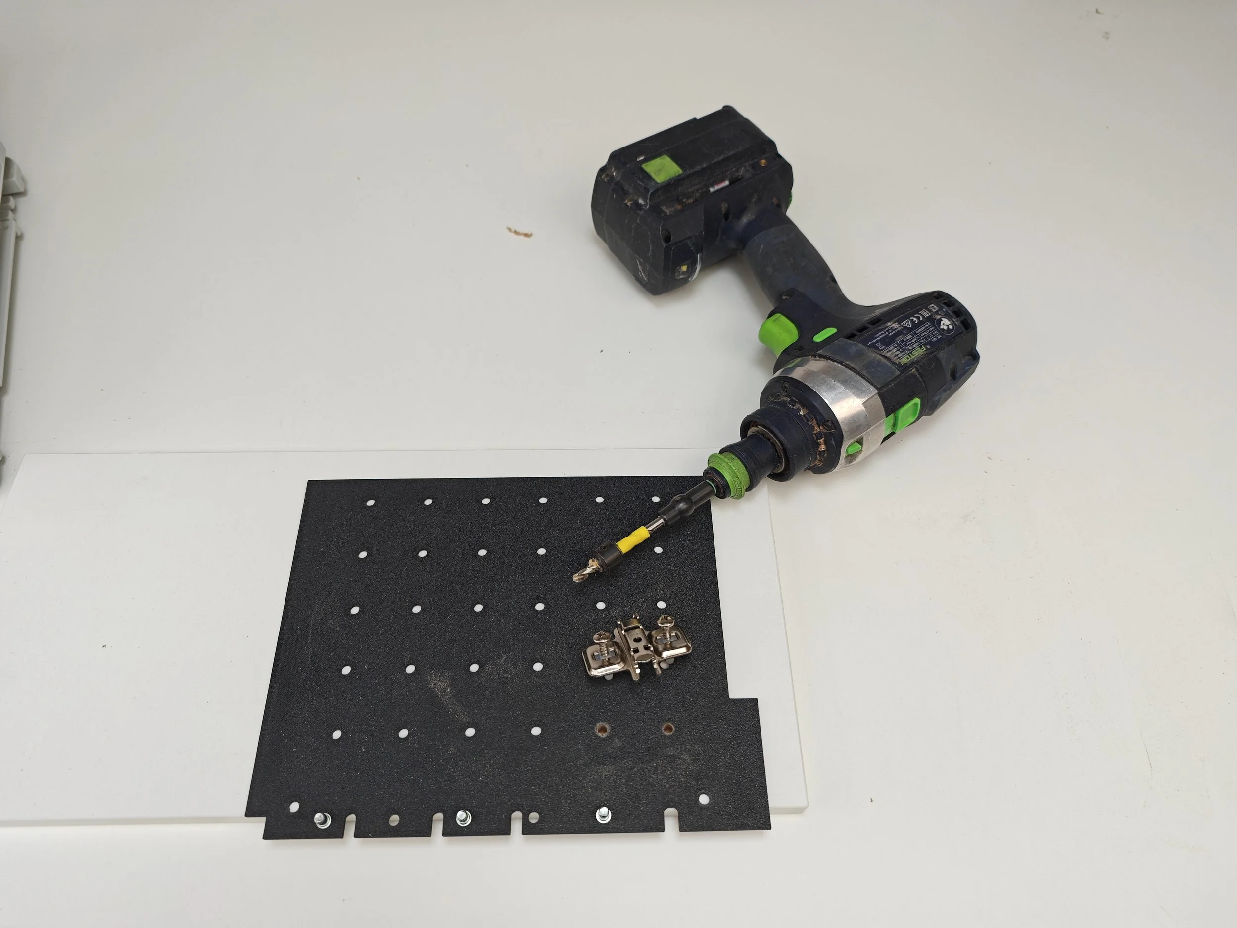 A power drill lying on a black perforated board with various metallic clips below it.