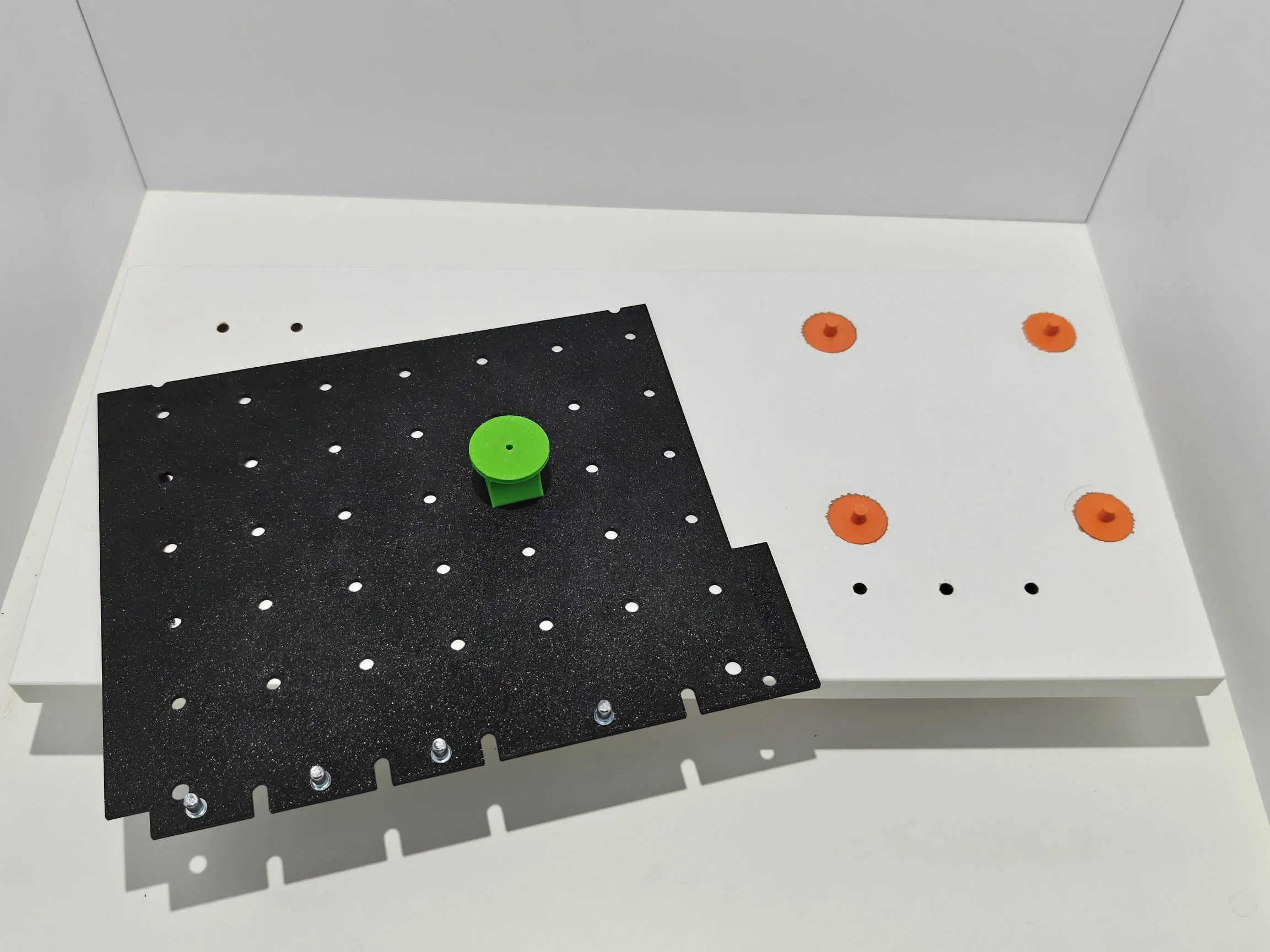 Assembly workspace with a black perforated board, orange and green spacers, and various screws on a white surface.