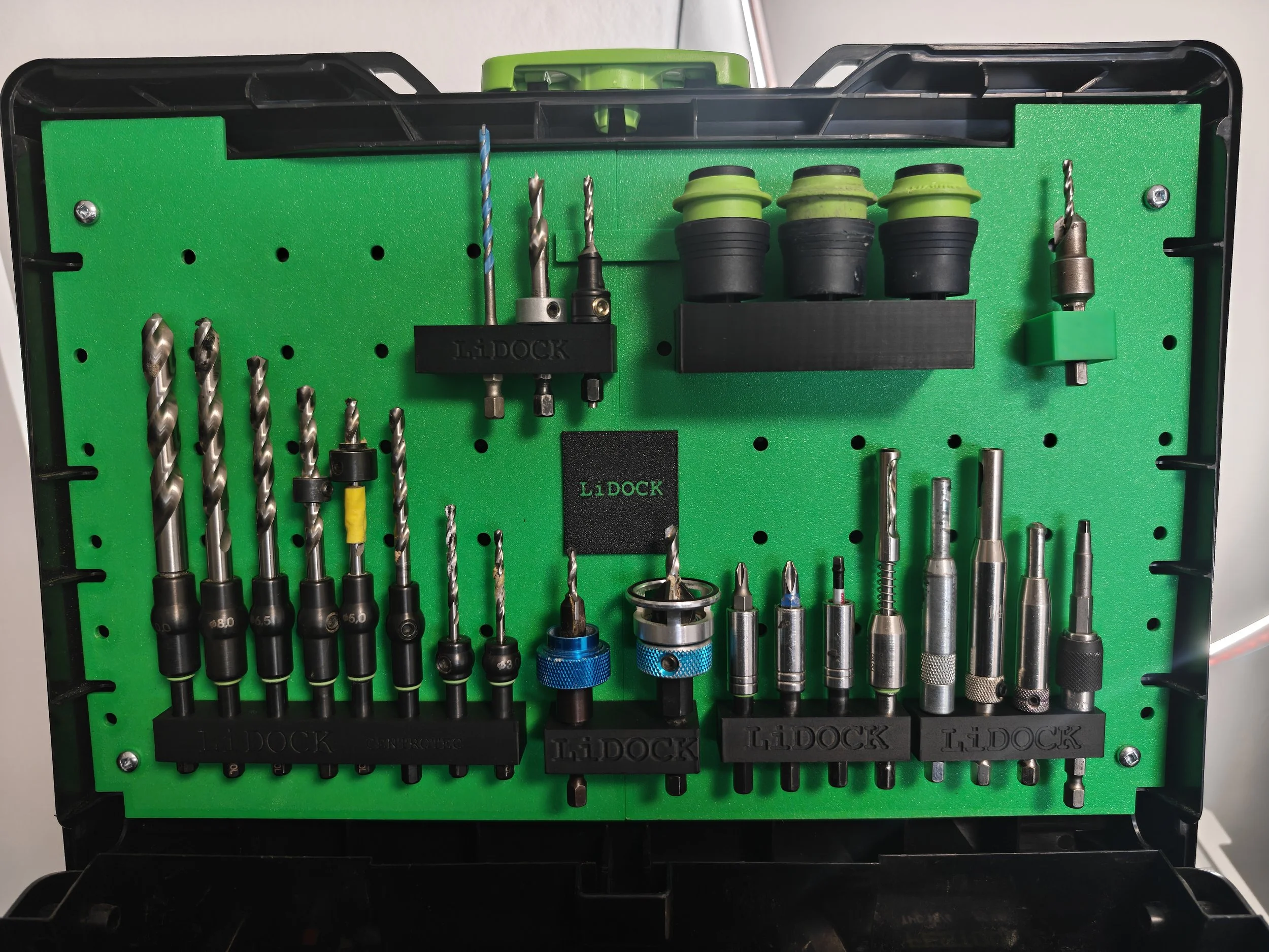 A green workbench organizer holding various drill bits, a drill chuck, and other tools.