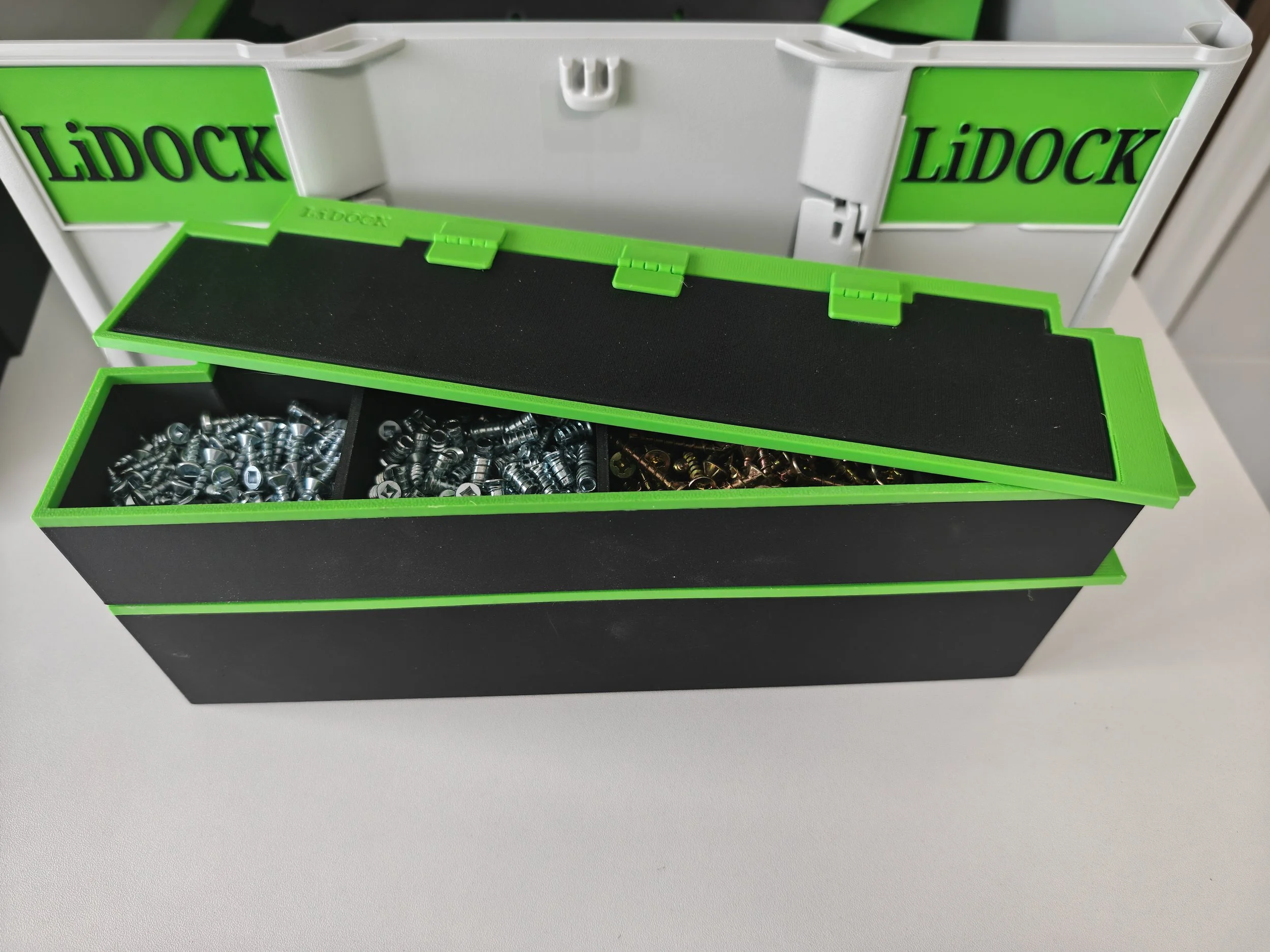 A black storage box with a green trim, containing metal hardware parts, placed on a white surface.
