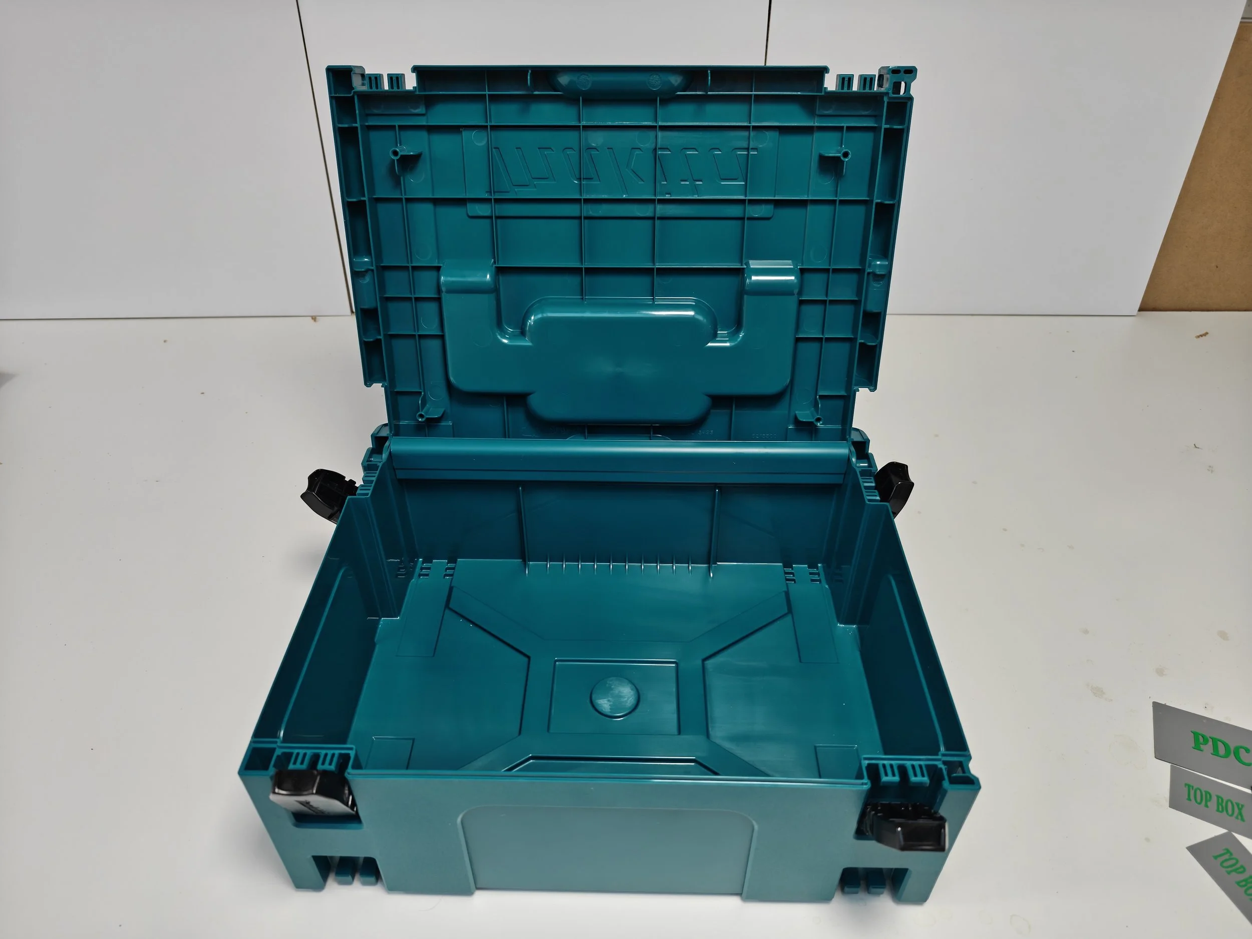 Open empty teal plastic storage box with black corner clasps on a white surface.